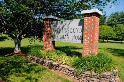 A stone sign reading Martin-Boyd Christian Home sits between brick pillars amid landscaped greenery.