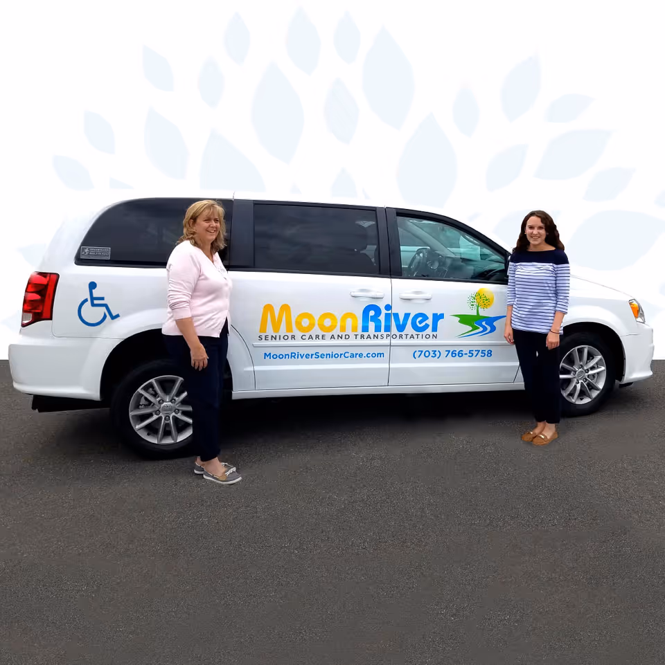 Two women stand beside a Moon River Senior Care van outdoors, smiling.