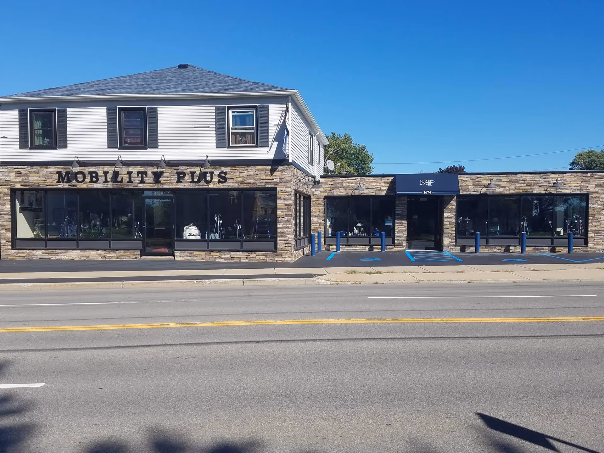 Exterior view of Mobility Plus facility along a street, with storefront windows and stone facade.