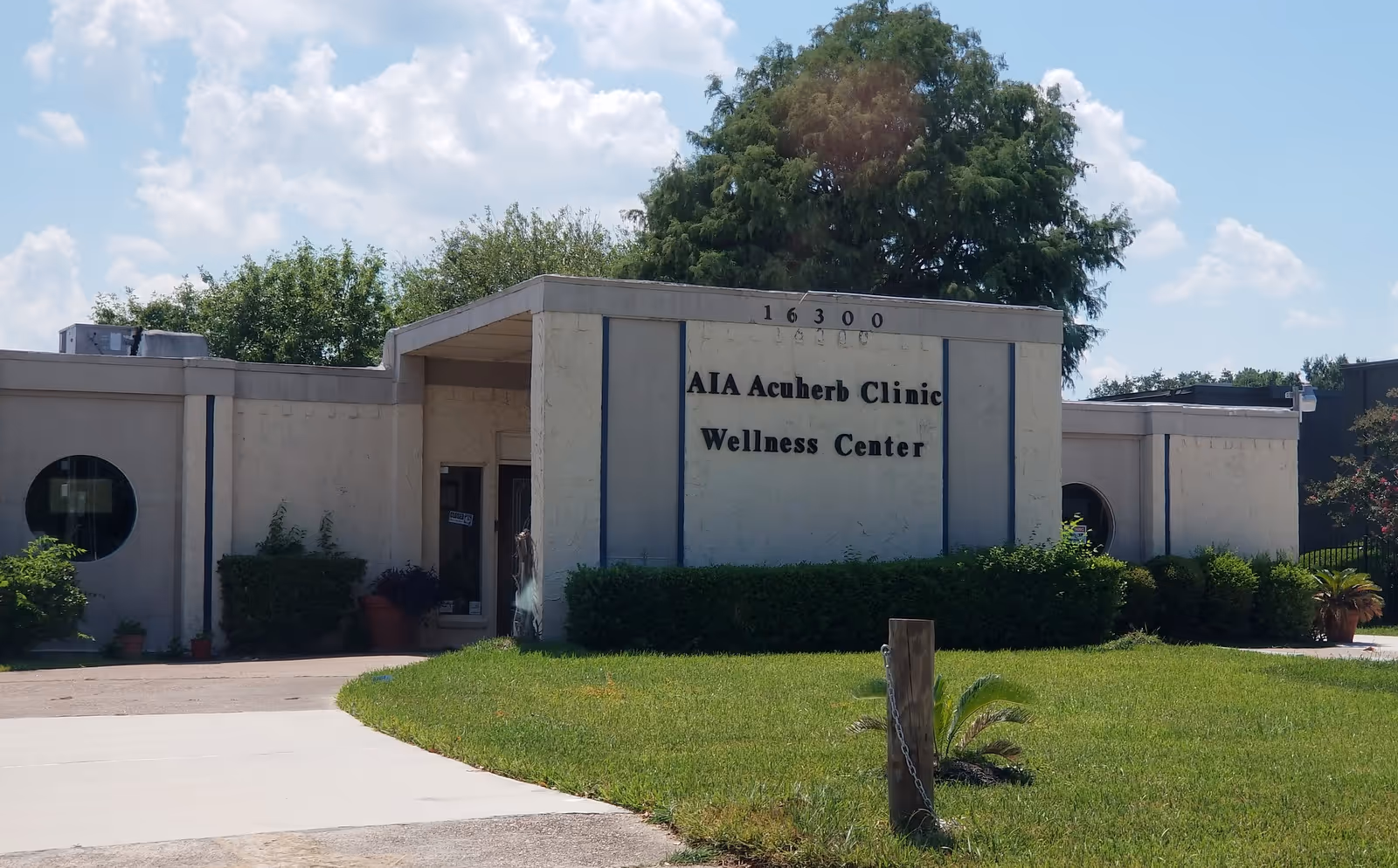 Exterior view of a white clinic building with AIA Acuherb Clinic Wellness Center sign.