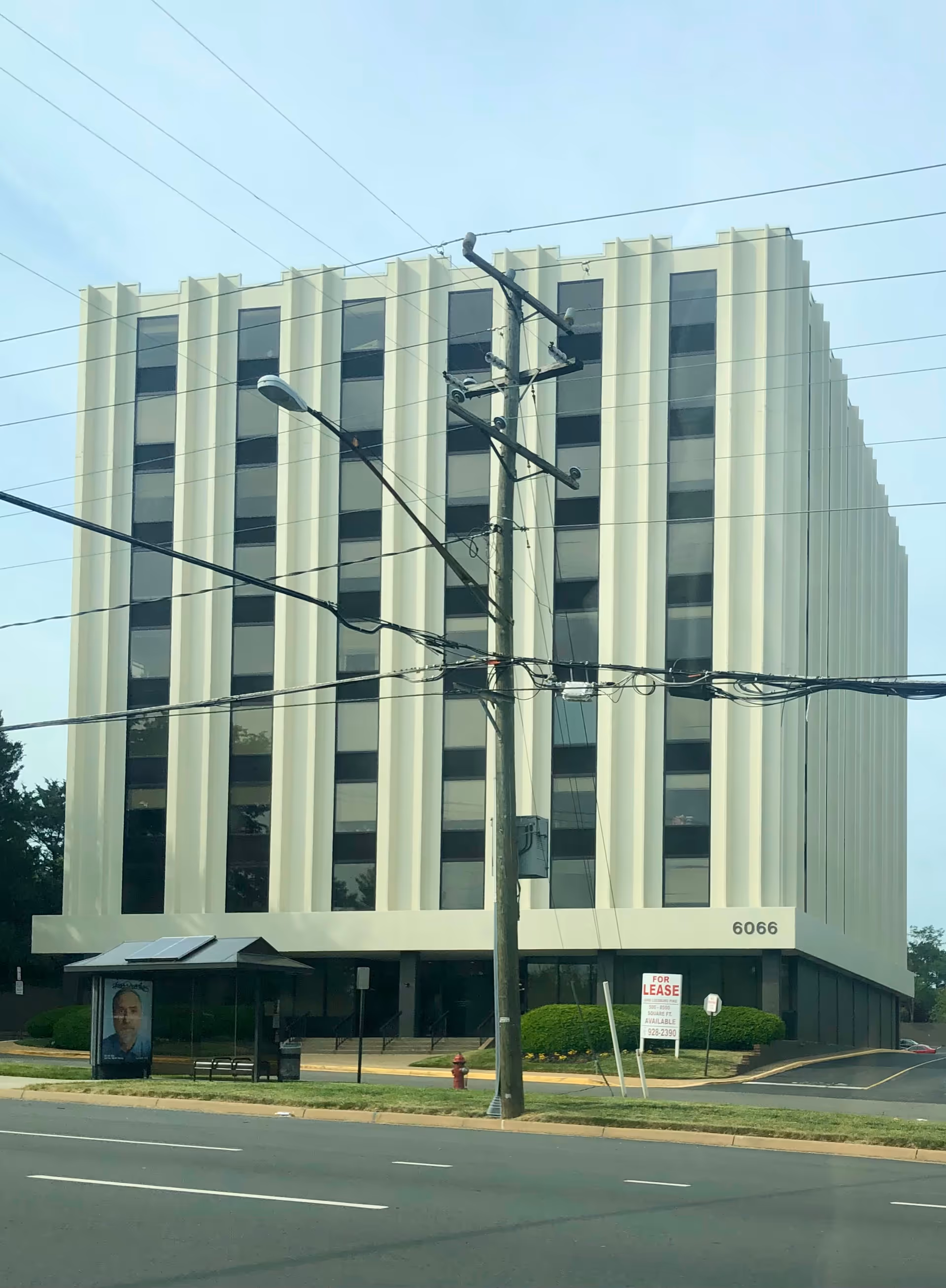 Tall modern building with vertical window bays along a street, power lines in front.