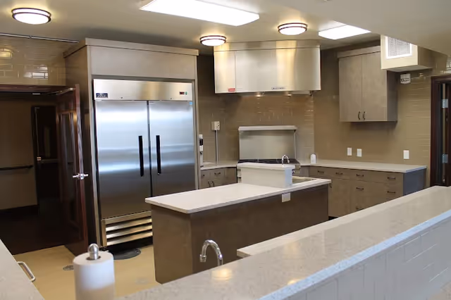 Industrial-style senior living facility kitchen with stainless steel appliances, countertops, and central island.