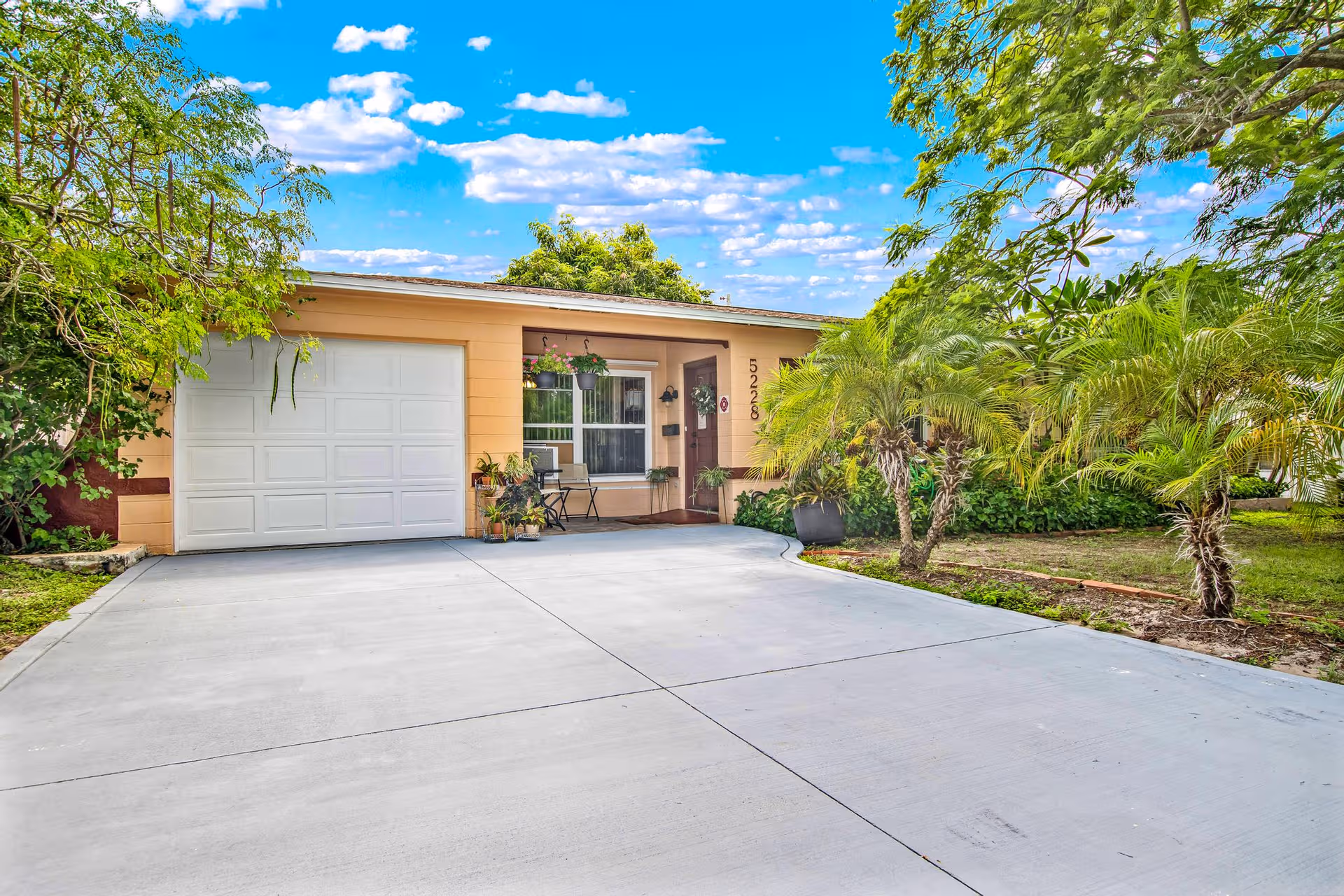 Front exterior of a single-story peach house with a large driveway and palm trees