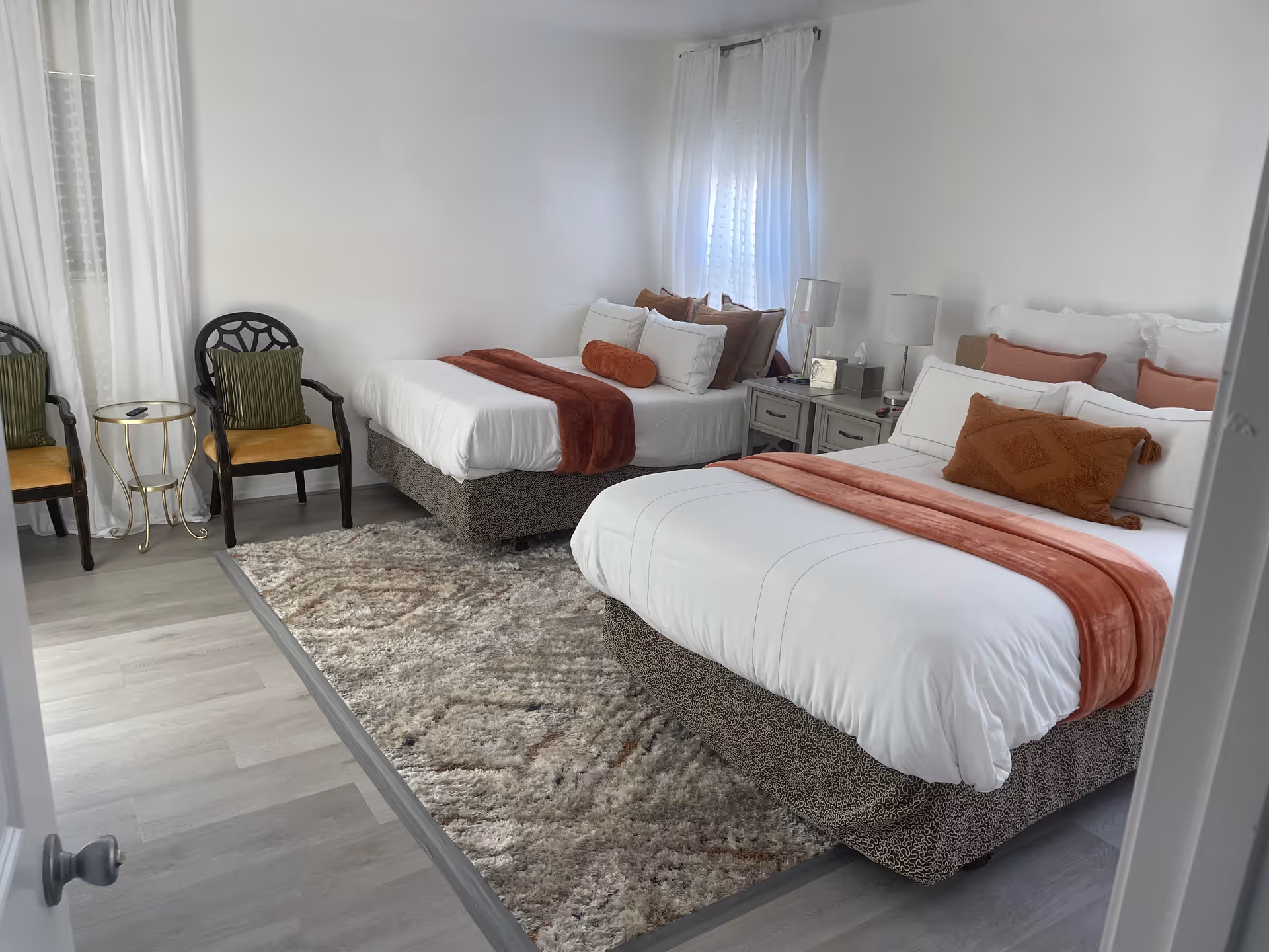 Two queen beds with white linens and orange accents in a well-lit bedroom.