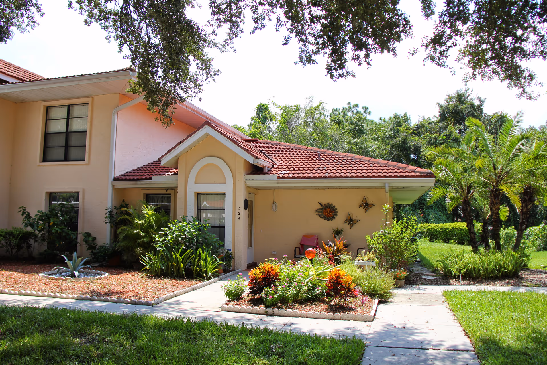 Front entrance of a peach-colored residence with a red tile roof, landscaped flower beds and a walkway.
