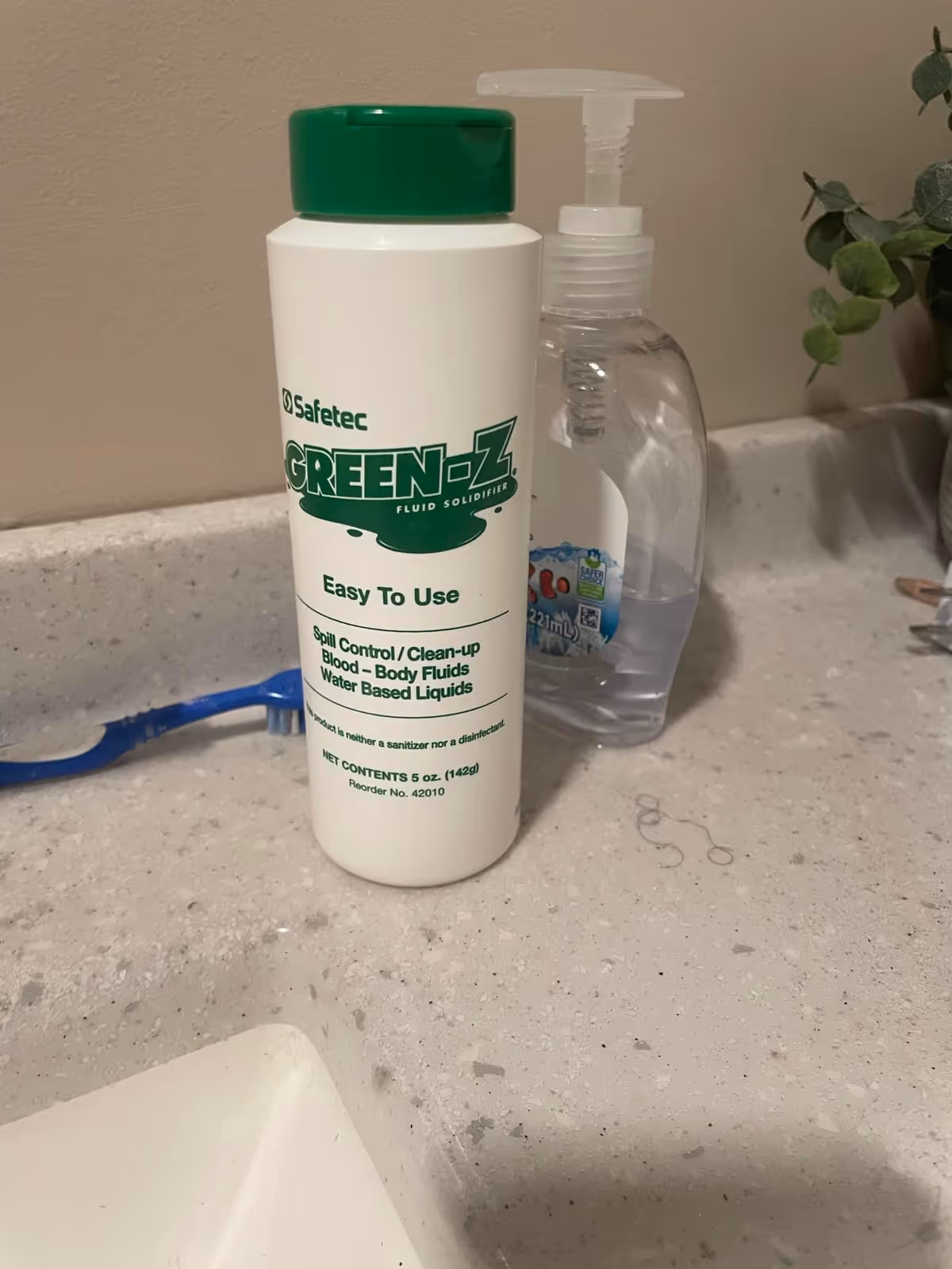 Bathroom counter with a Green-Z cleaning bottle, hand sanitizer dispenser, toothbrush, and a small plant.