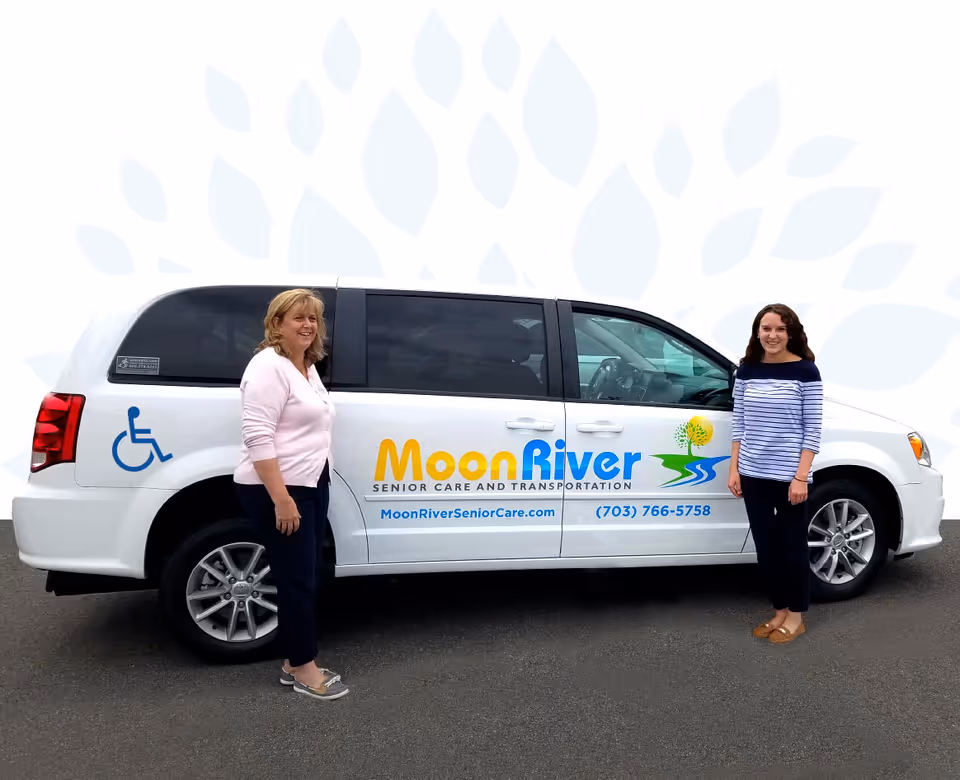 Two women stand beside a white Moon River senior care van with wheelchair symbol.