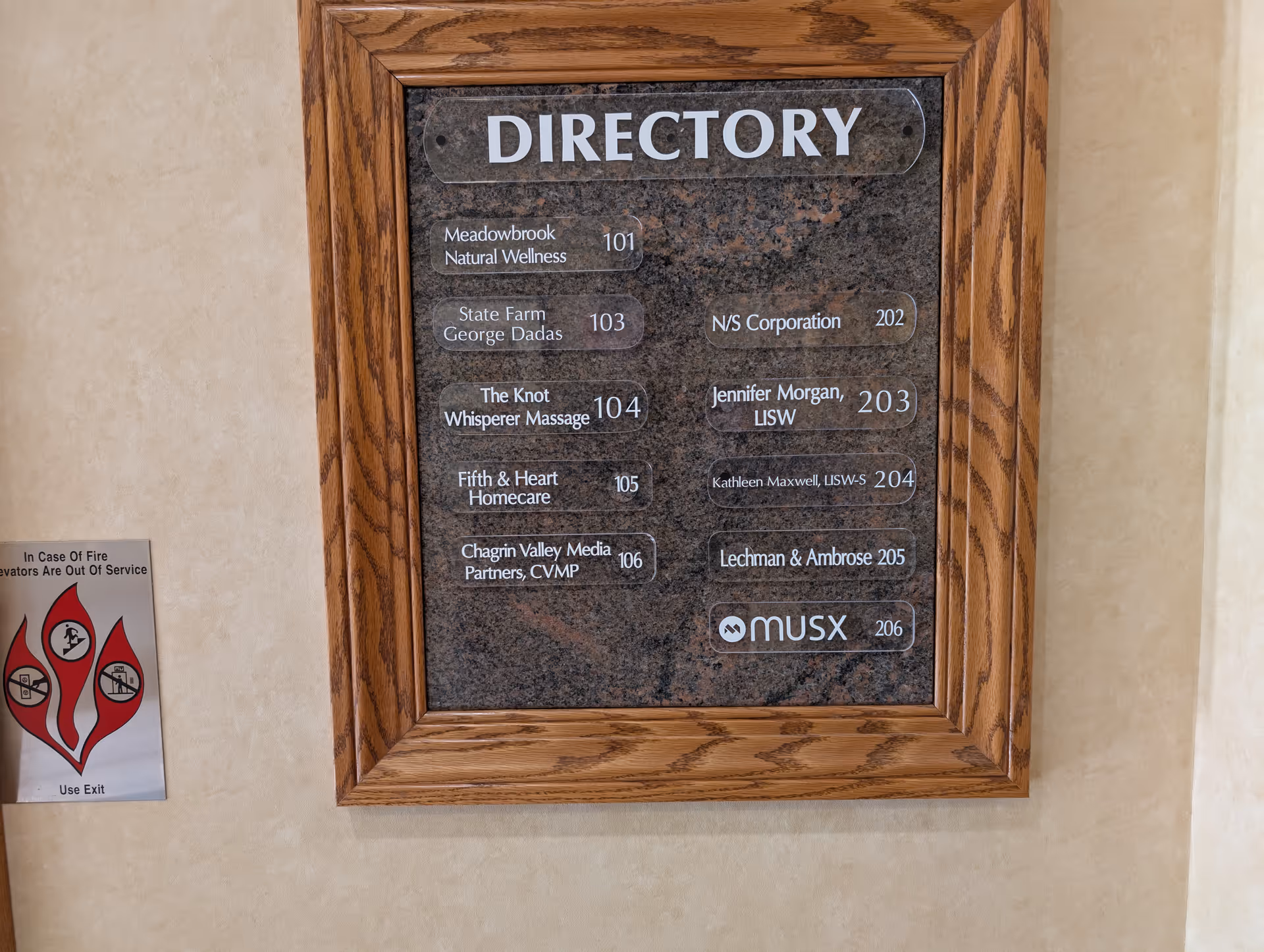 Beige hallway wall with a wood-framed directory plaque listing tenants at Fifth and Heart Homecare.