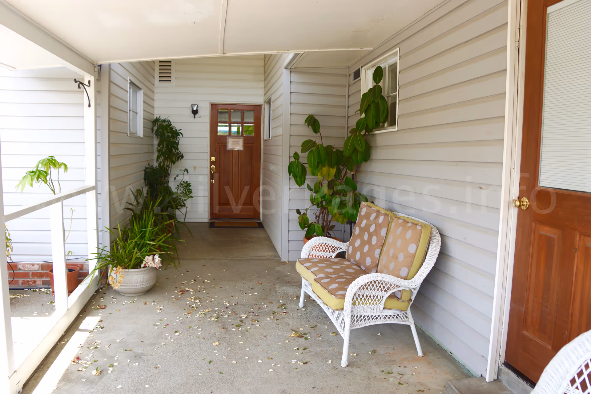 Covered outdoor entry with wicker bench, potted plants, and a wooden door.