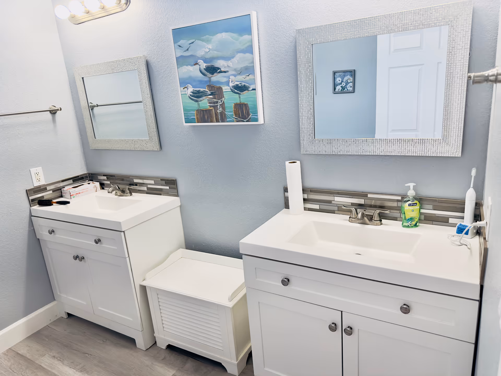 Two white bathroom vanities with sinks and mirrors in a light blue room.