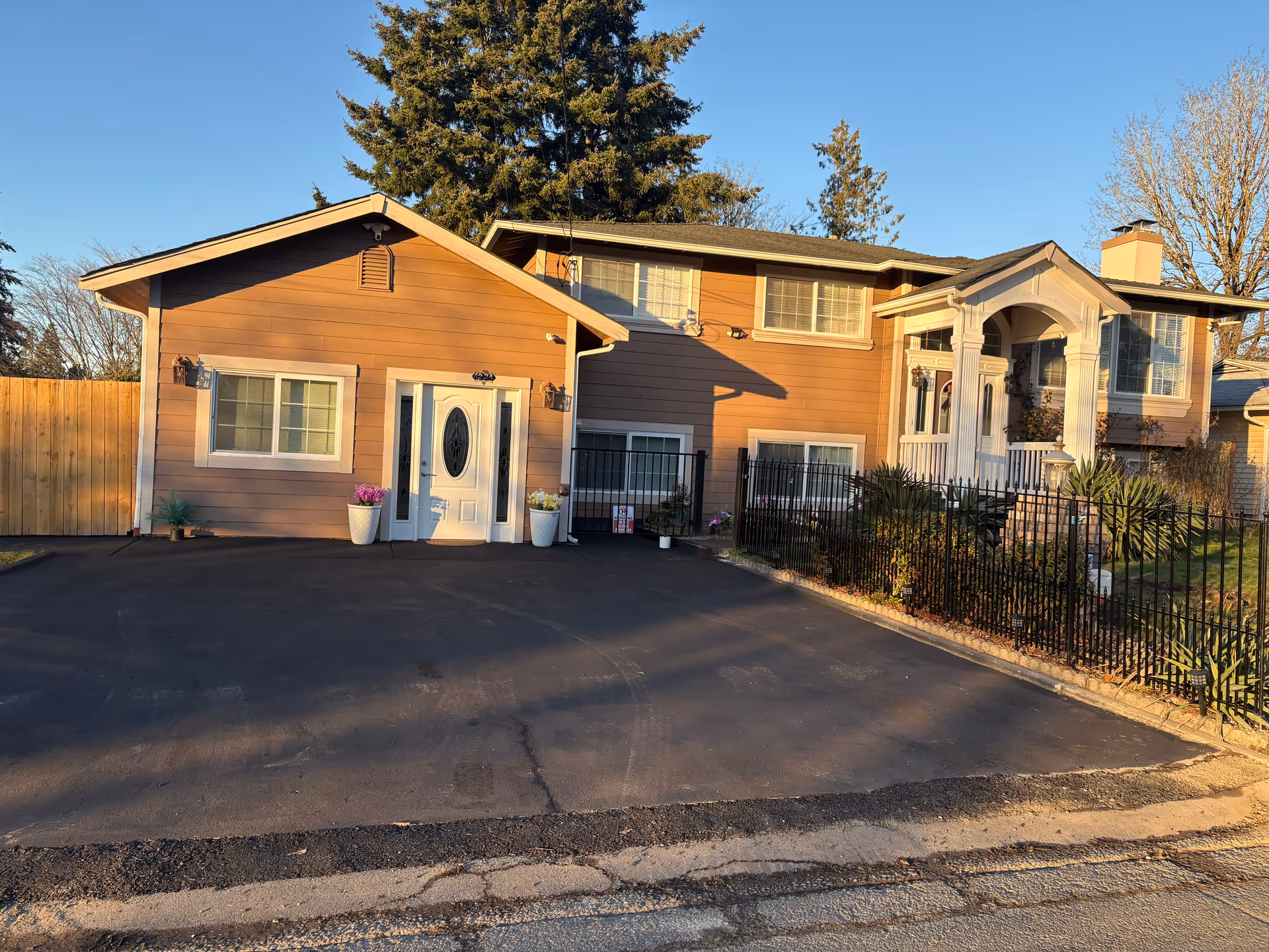 Two connected residential buildings with a paved driveway and a wrought-iron fence.