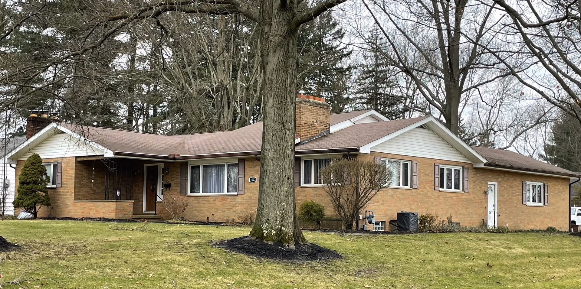 Single-story brick facility with a peaked roof, expansive lawn, and a large front tree.