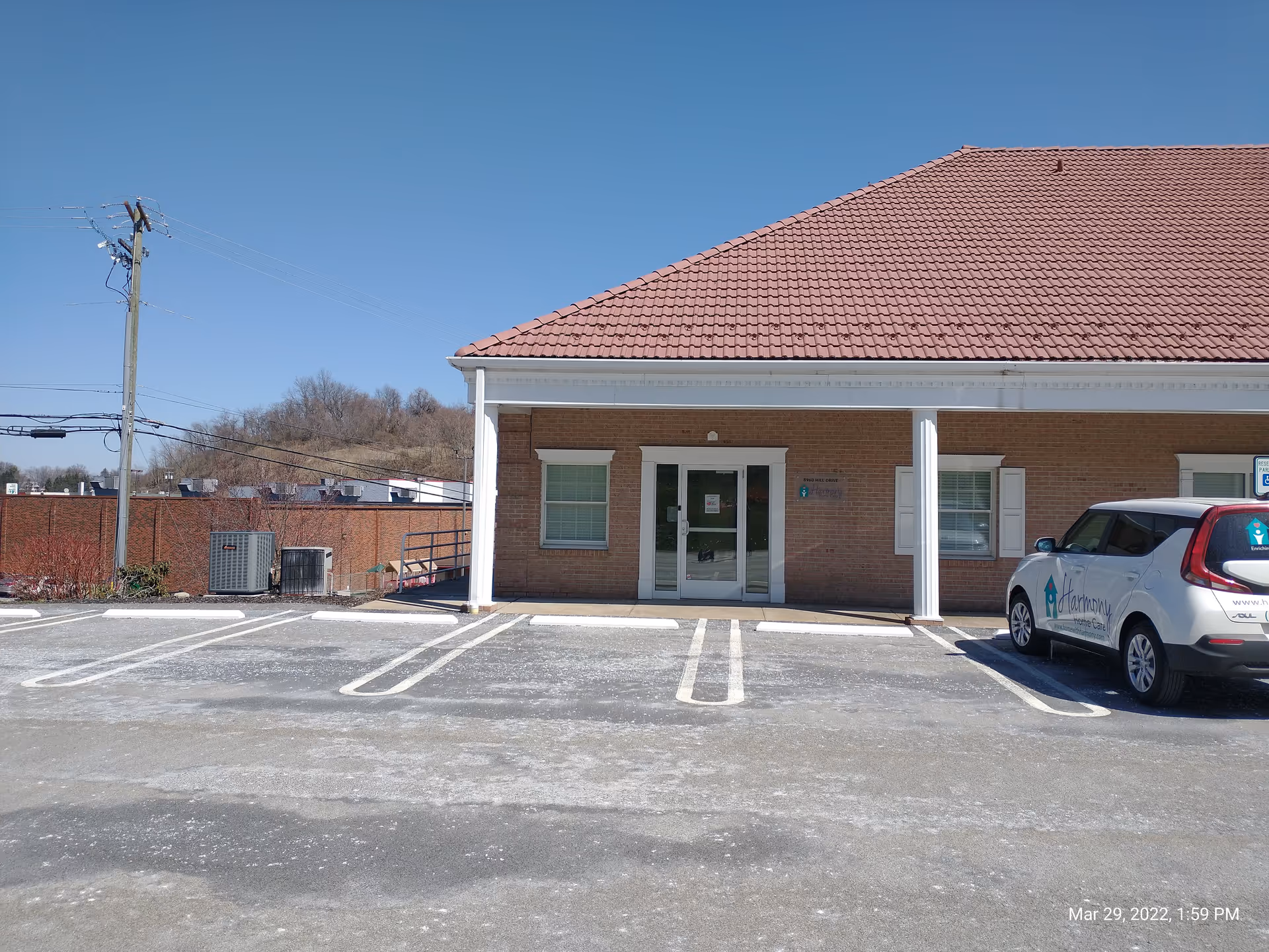 Brick building with red-tiled roof and glass entrance, parking lot, and a white vehicle.