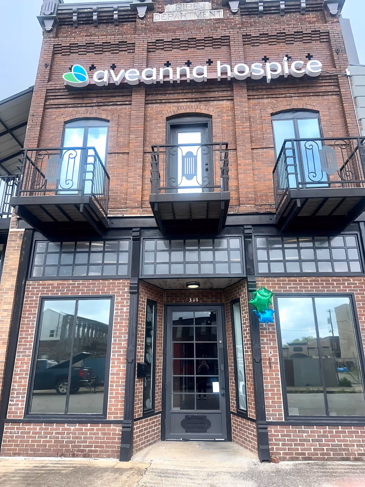 Brick-front Aveanna Hospice building with glass entrance and upper story balconies.