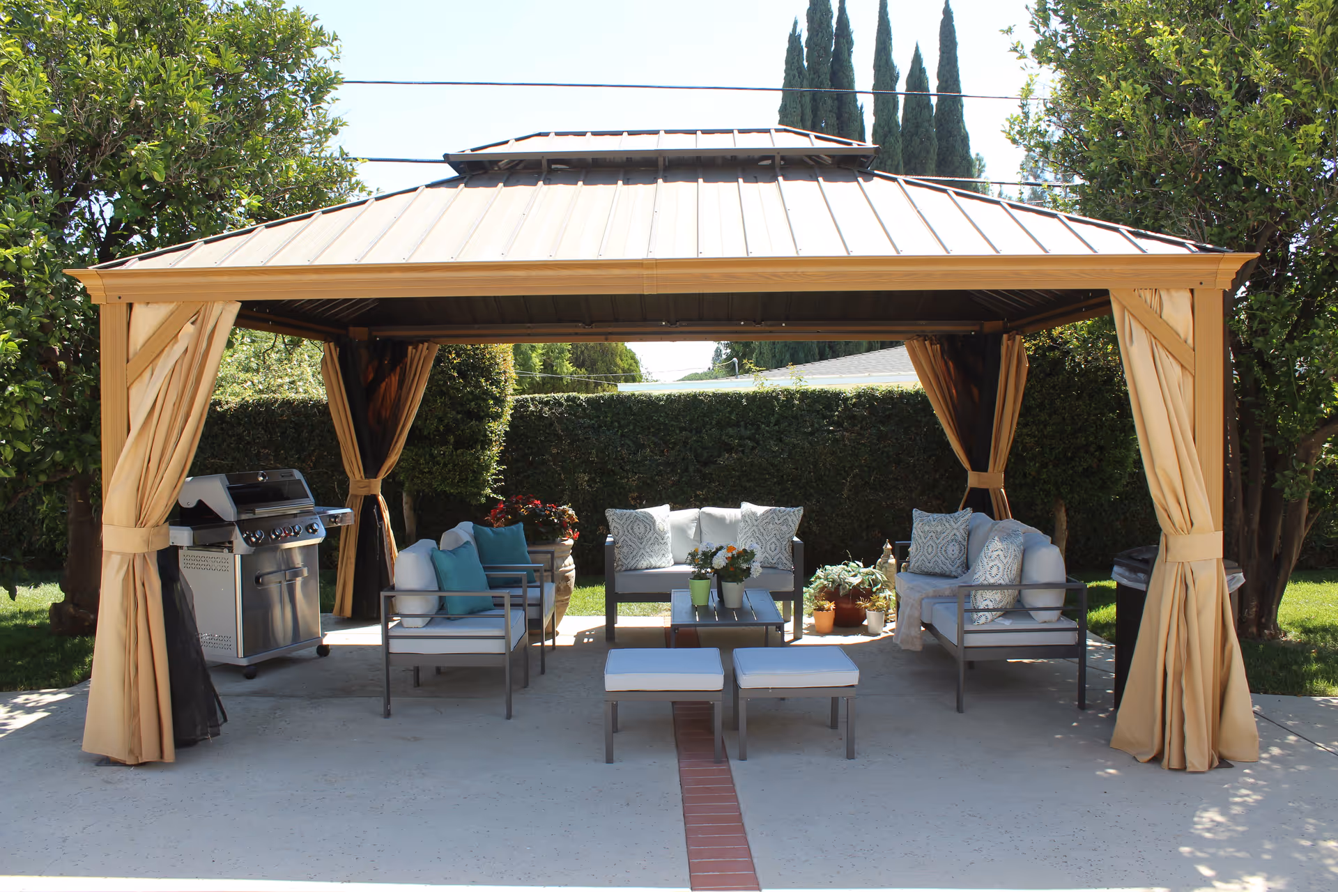 Outdoor living area with cushioned seating under a beige canopy and a grill.