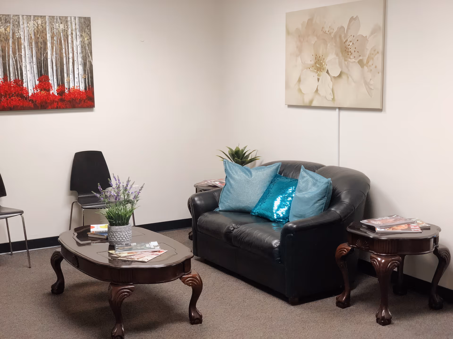 Cozy indoor waiting area with a black leather sofa and teal cushions.