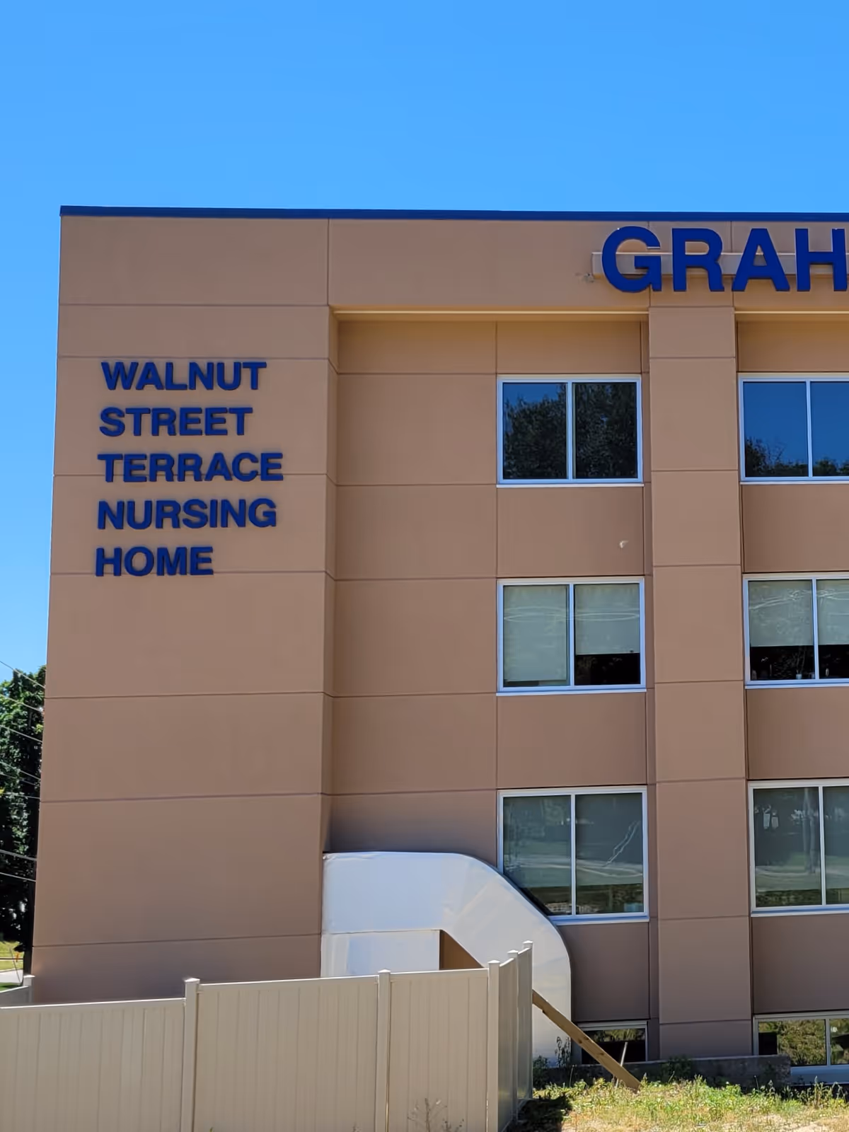 Exterior view of a tan, multi-story nursing home building with blue signage.