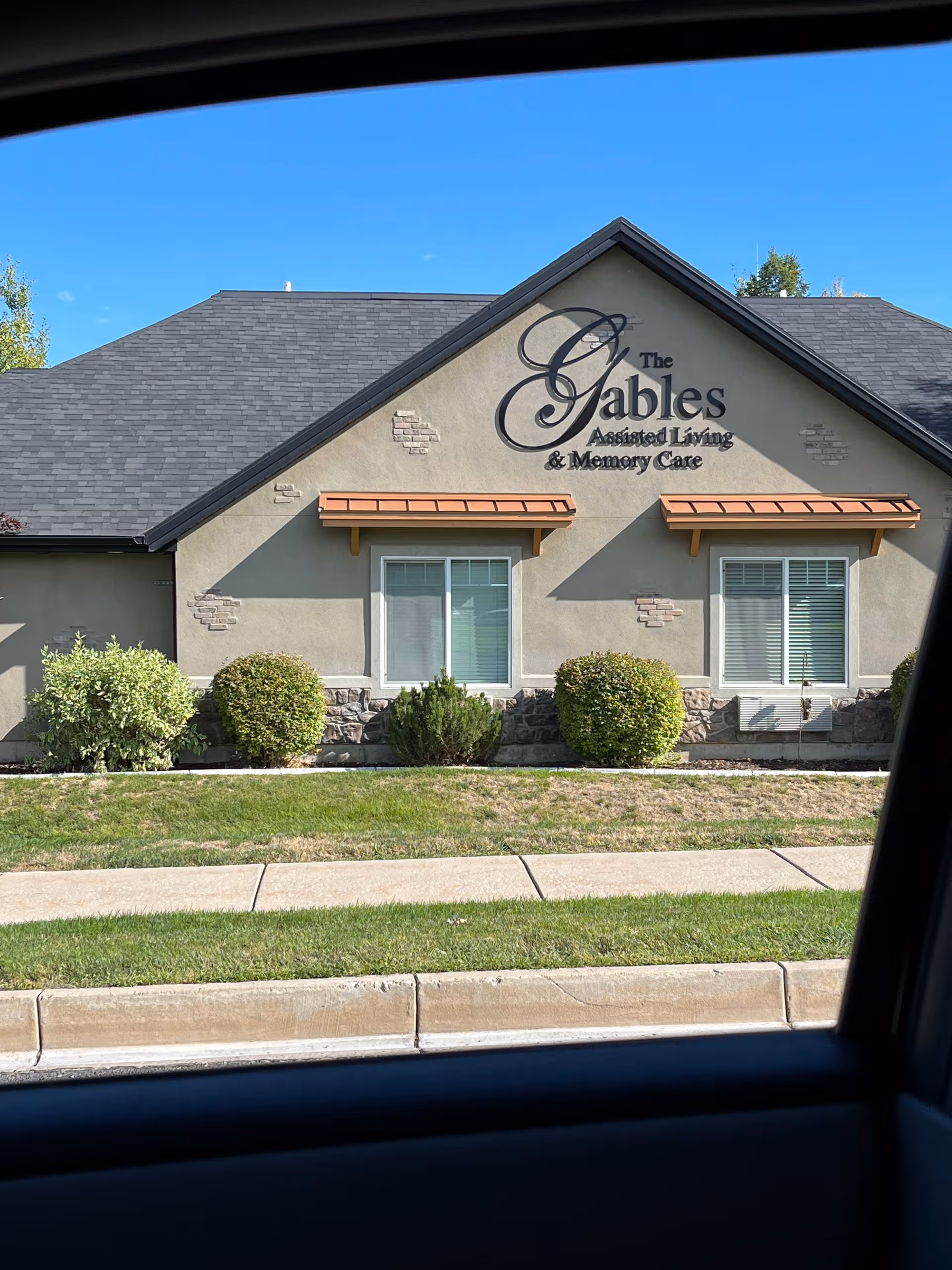 Front view of The Gables Assisted Living building with sign and shrubs.