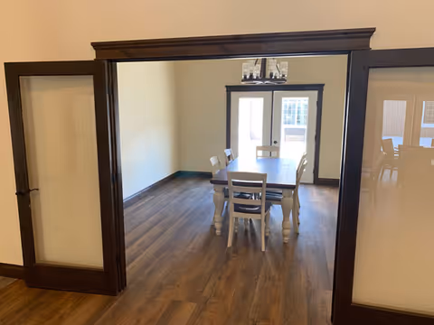 Interior dining room with a wooden table and chairs through a dark doorway.