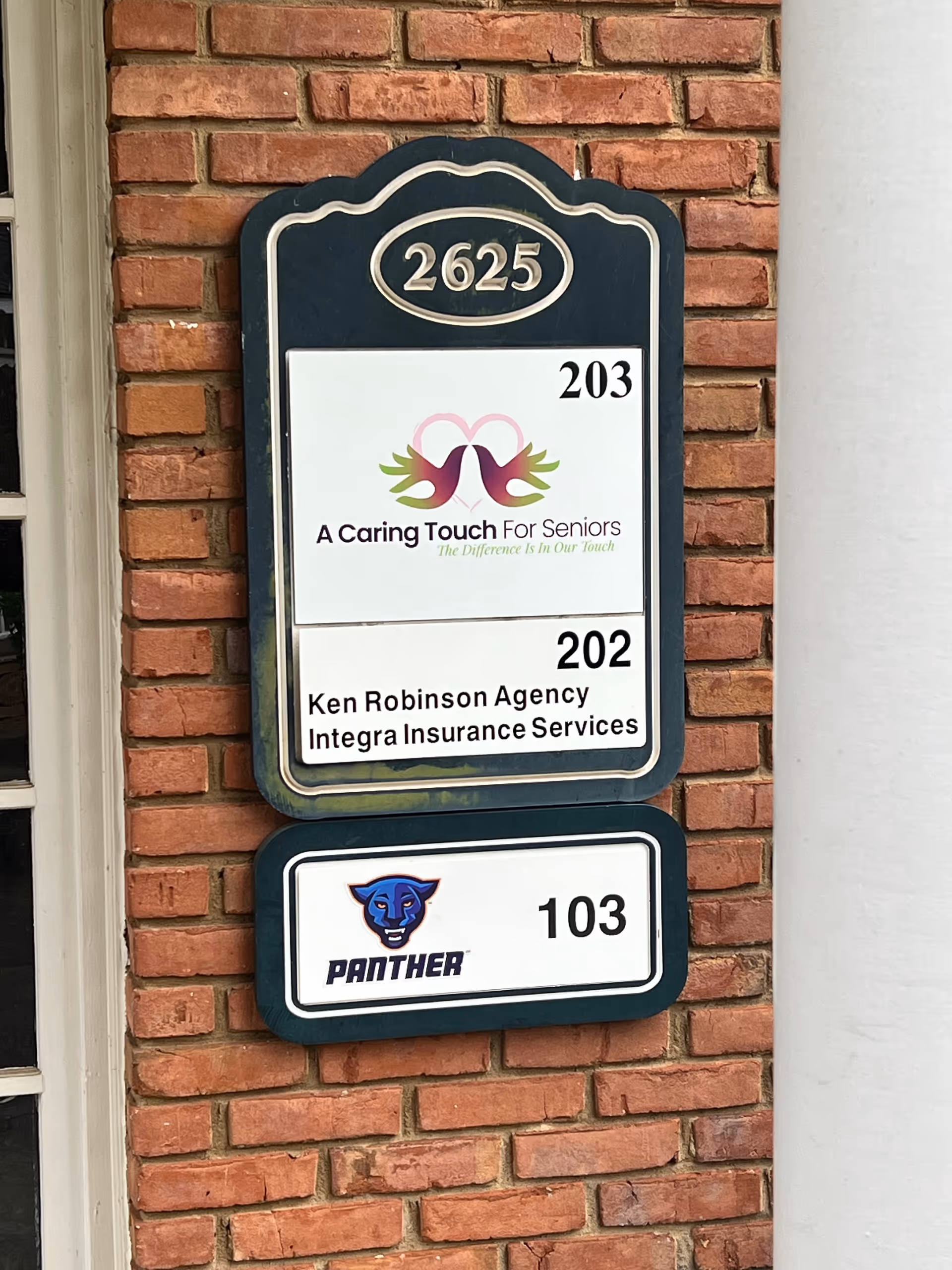 Brick wall directory sign displays numbers and logos, including A Caring Touch For Seniors.