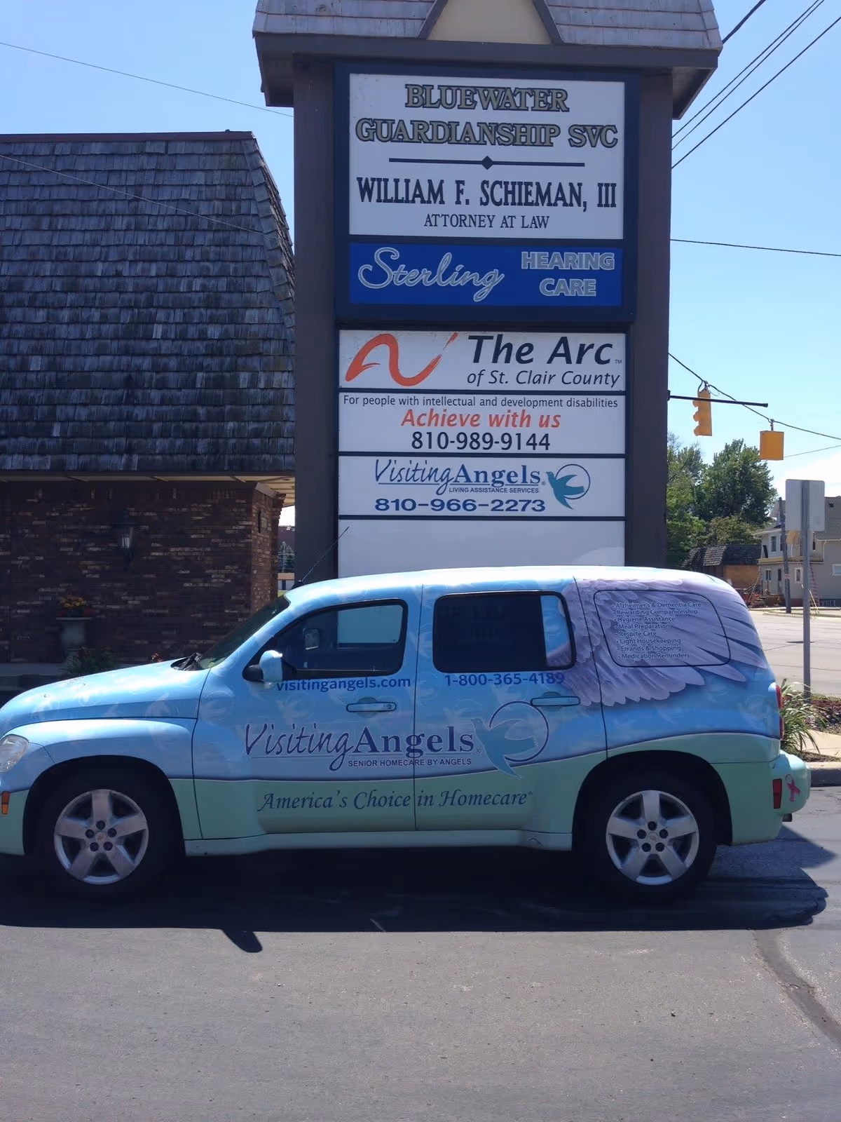 Blue and white Visiting Angels van parked beside a tall multi-sign storefront in Port Huron.