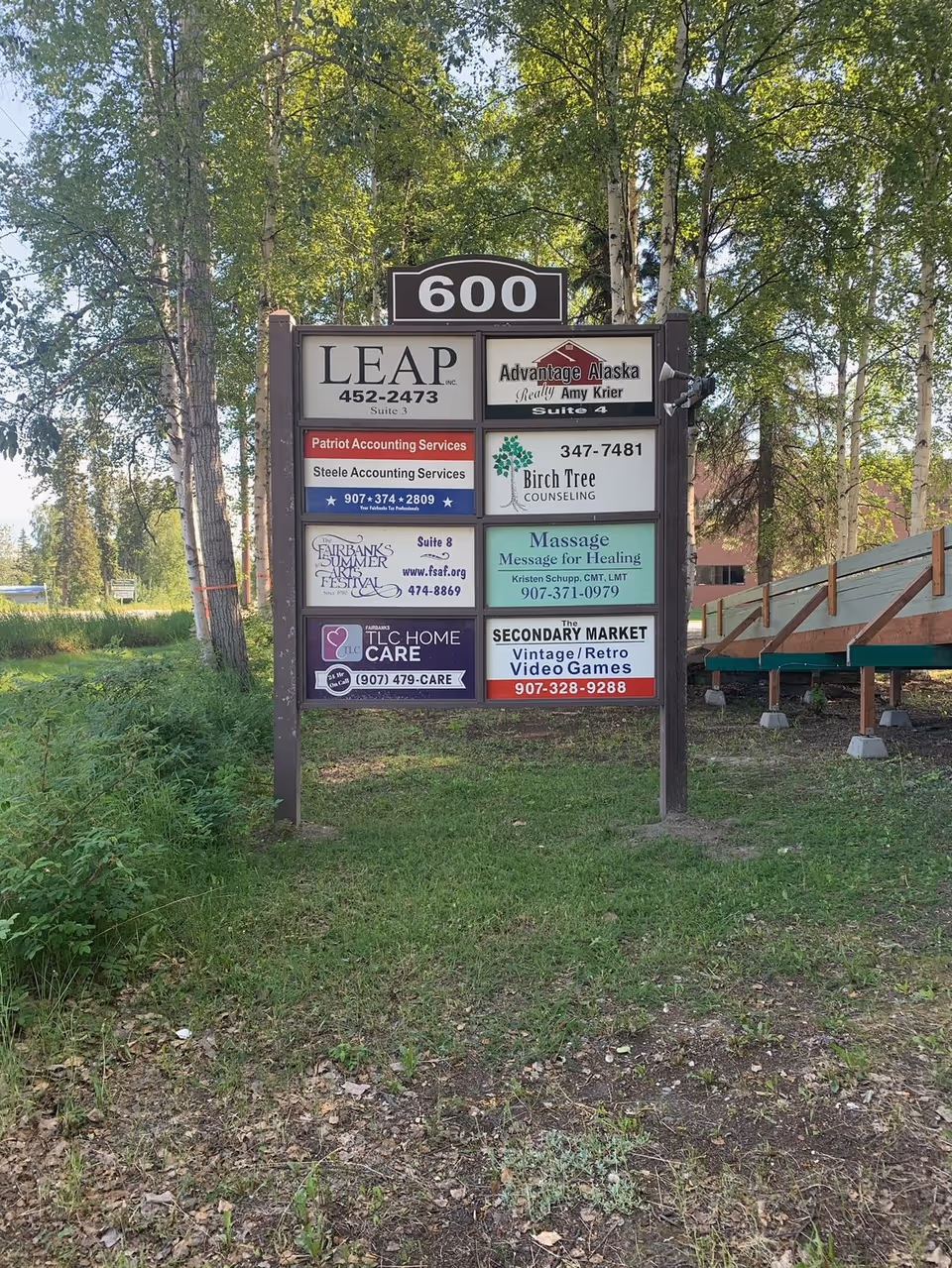 Outdoor directory sign listing TLC Home Care among multiple neighboring businesses in a green area.