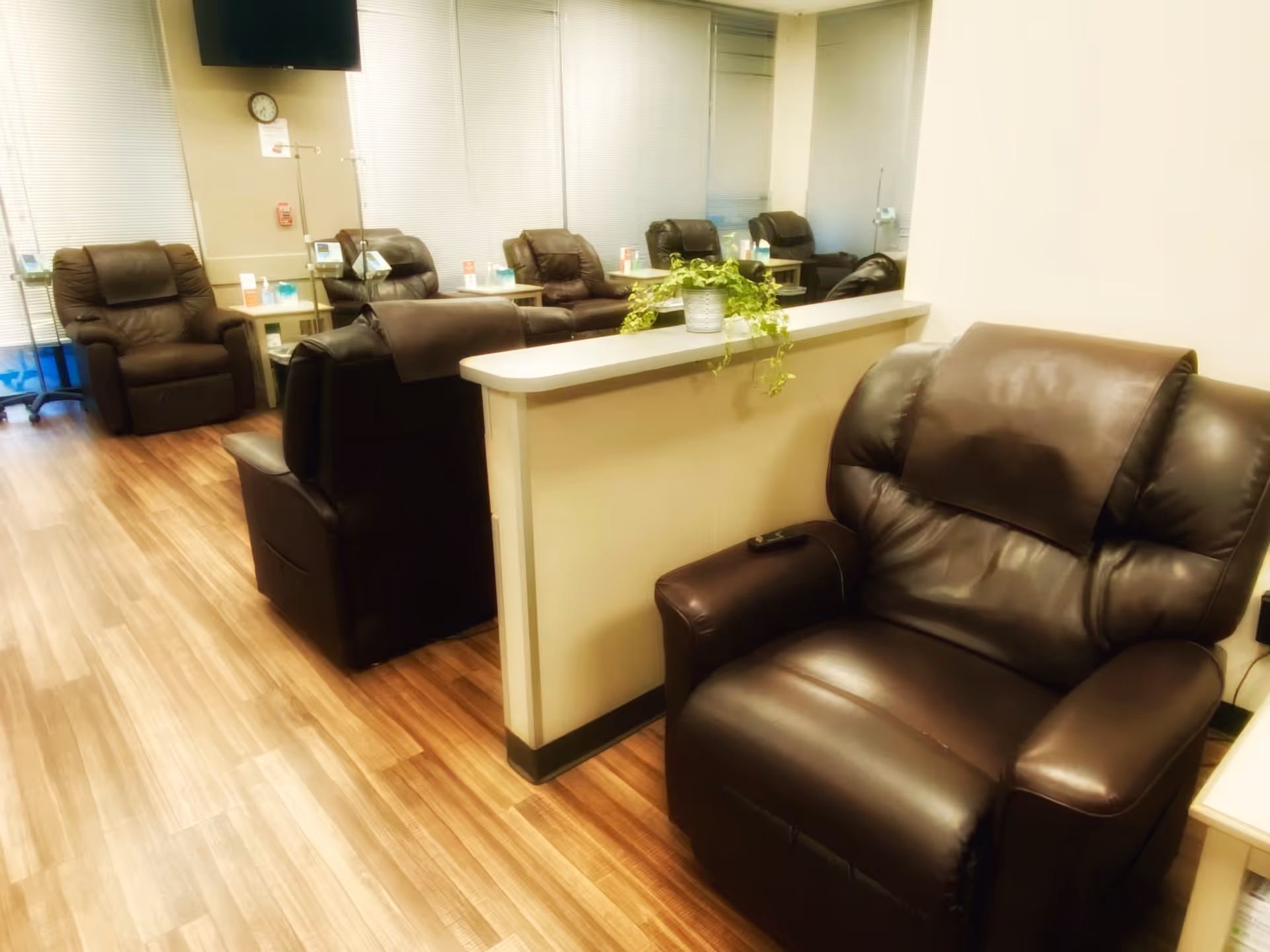 Infusion center lounge with brown leather recliners, a half-wall counter, and potted plants.