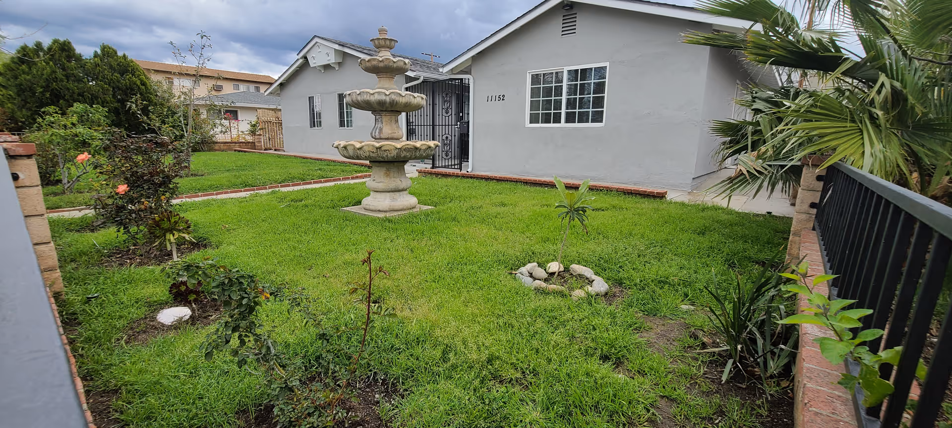Exterior view of Alalik Care Home showing a fountain, lawn, and surrounding plants.