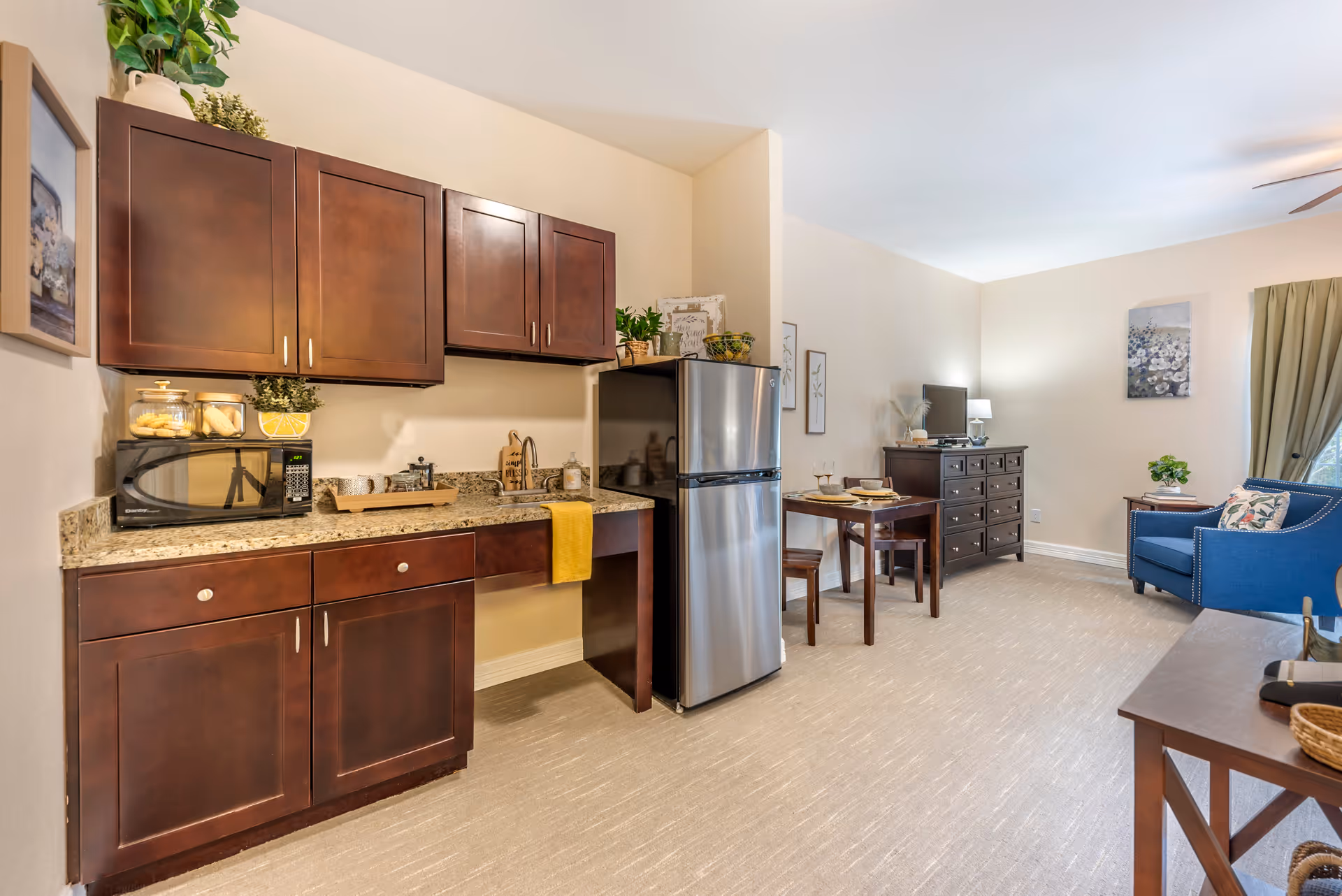 Open-concept kitchenette and living area of Brookdale Beckett Meadows with dark wood cabinets.