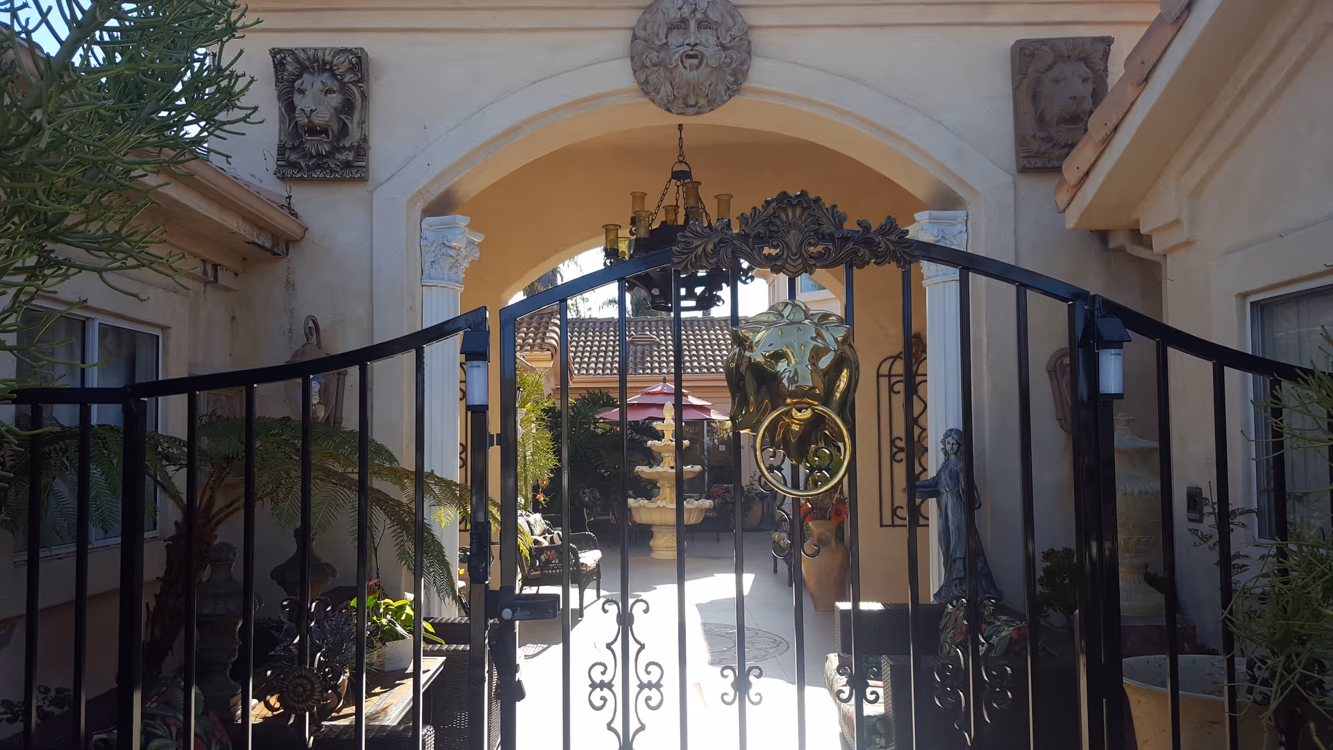 Ornate courtyard entrance with iron gate, statues, and potted plants at Alta Vista Manor.