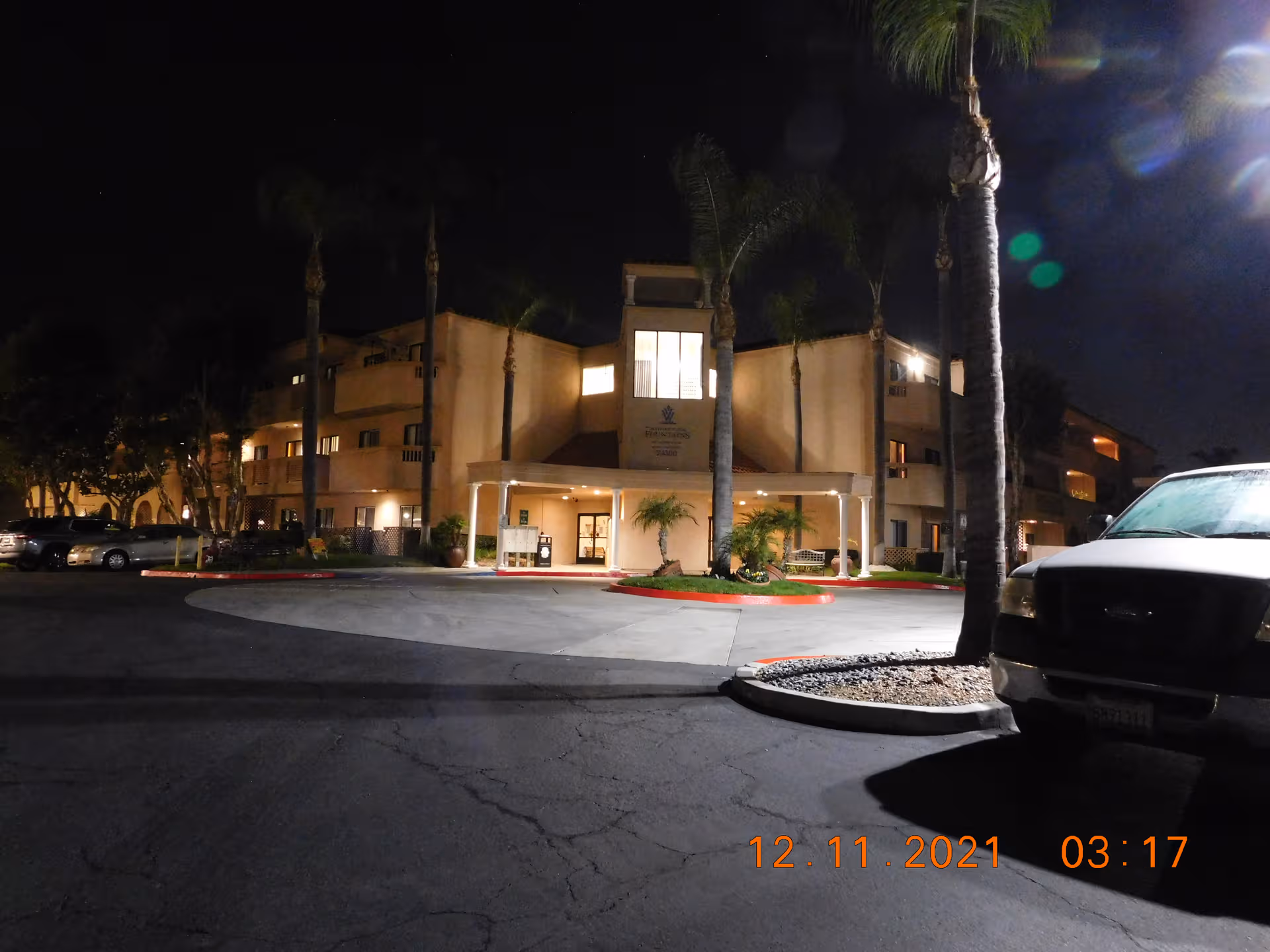 Night exterior view of Whispering Fountains Laguna Woods with illuminated entrance and palm trees