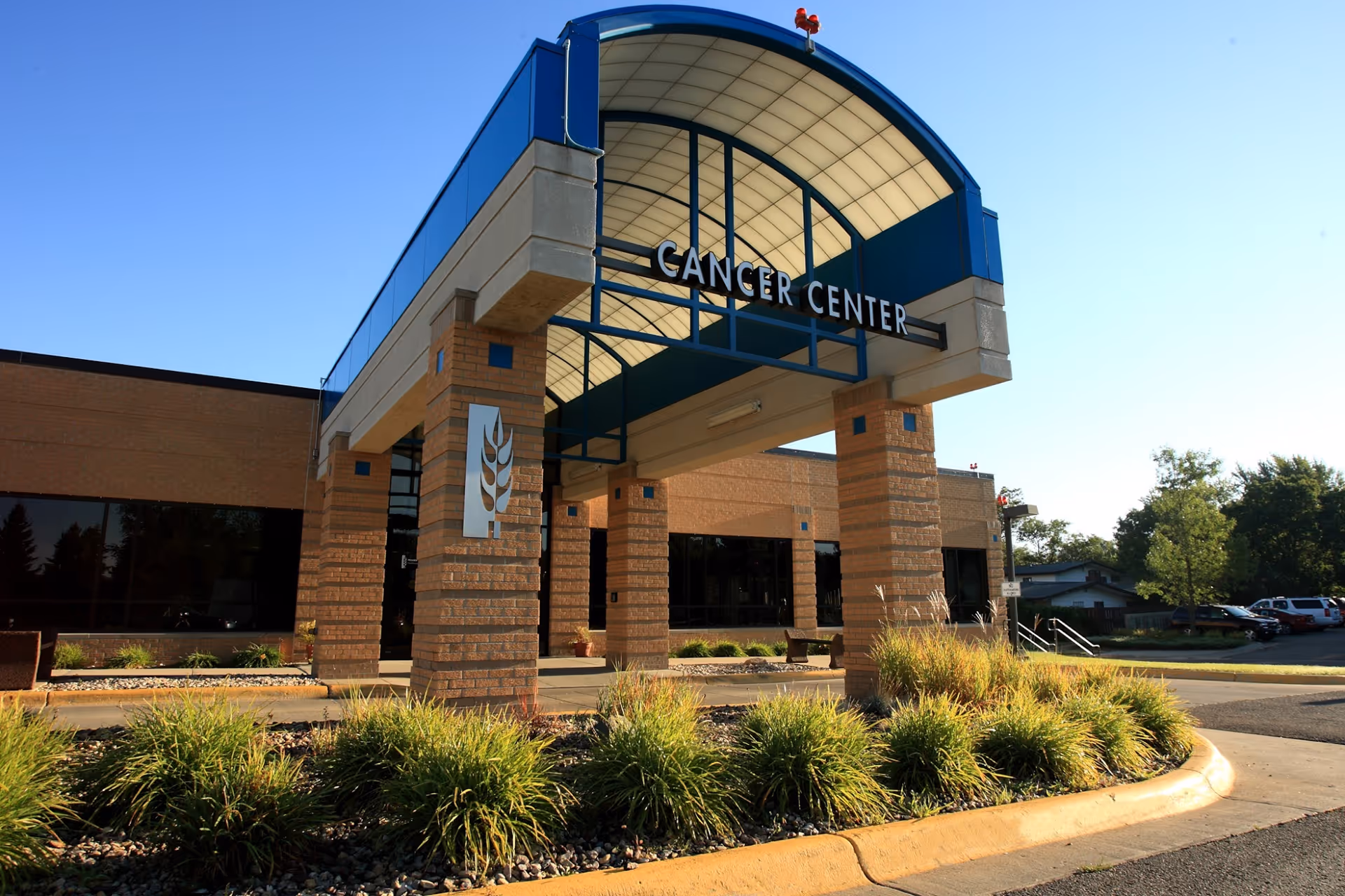 Exterior view of a cancer center entrance with brick columns and a curved blue canopy.