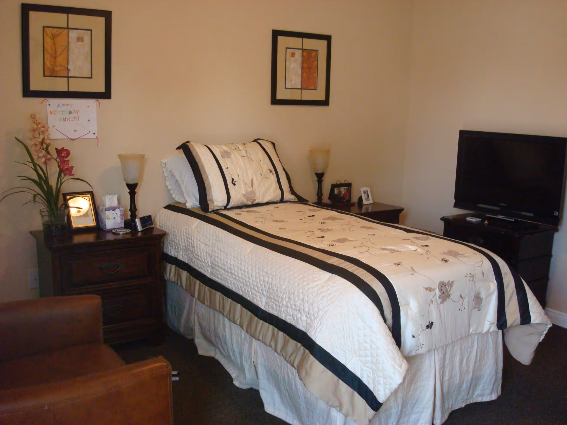 A neatly made bed with matching nightstands and a TV in a cozy senior living bedroom.