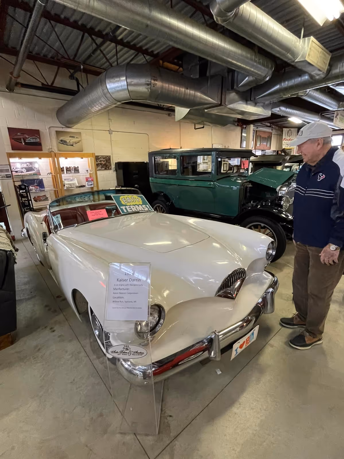 Indoor showroom with vintage cars and a man examining a white convertible.