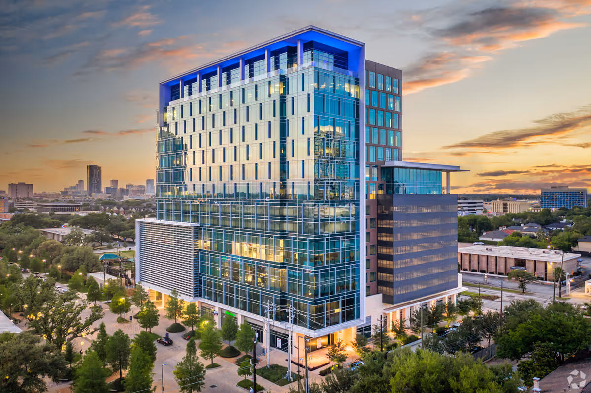 A modern glass-front building exterior at sunset with surrounding trees.