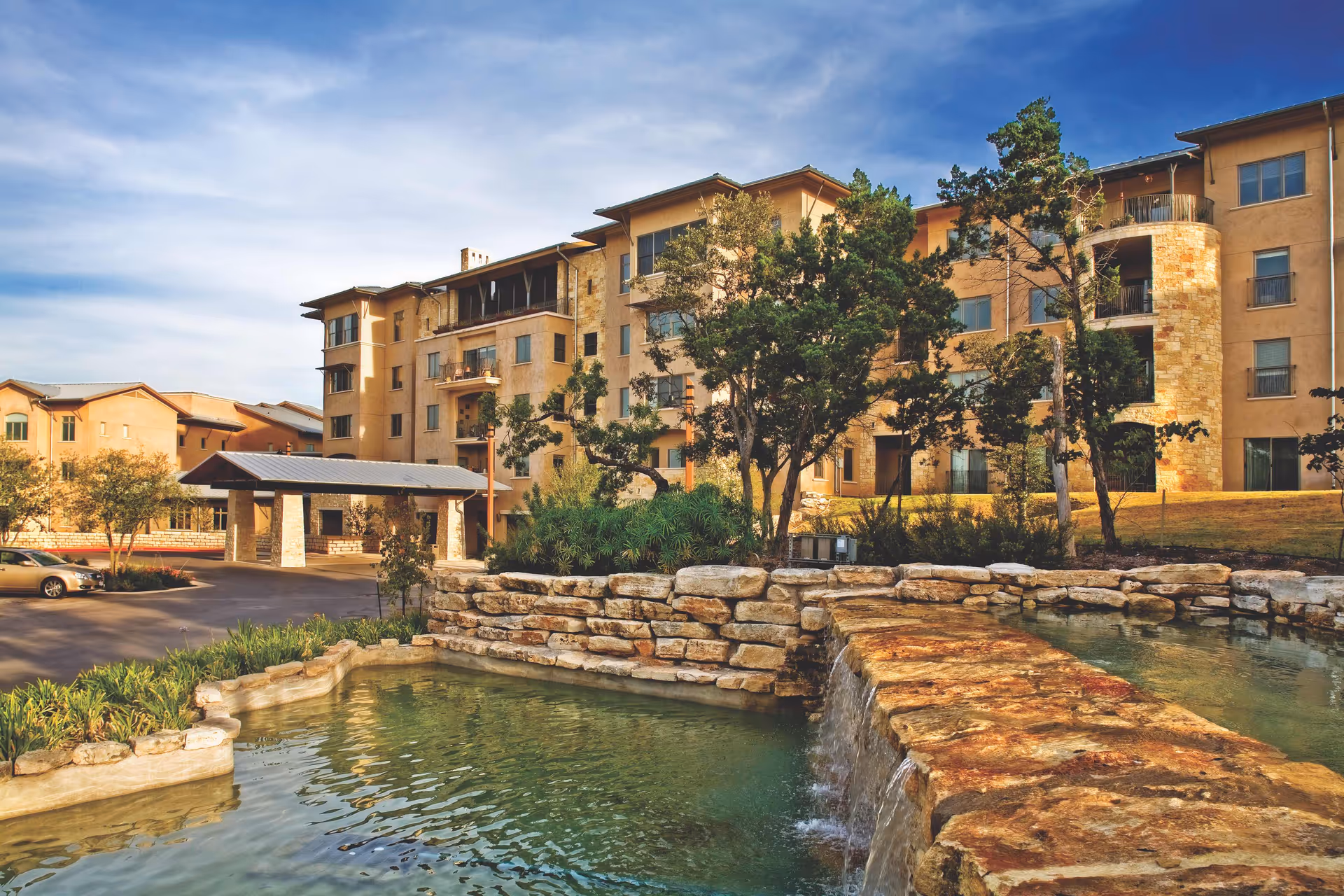 Exterior view of a multi-story senior living building with a stone water feature.