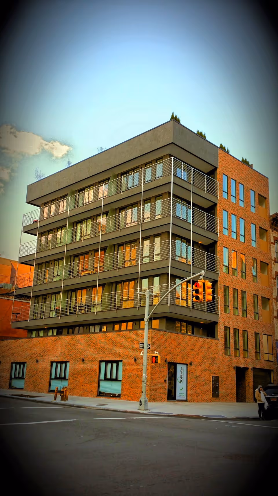 Modern multi-story brick-and-gray building with metal balconies along a city street.