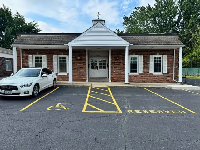 Brick senior living facility with white columns, front entrance, and a reserved parking area.