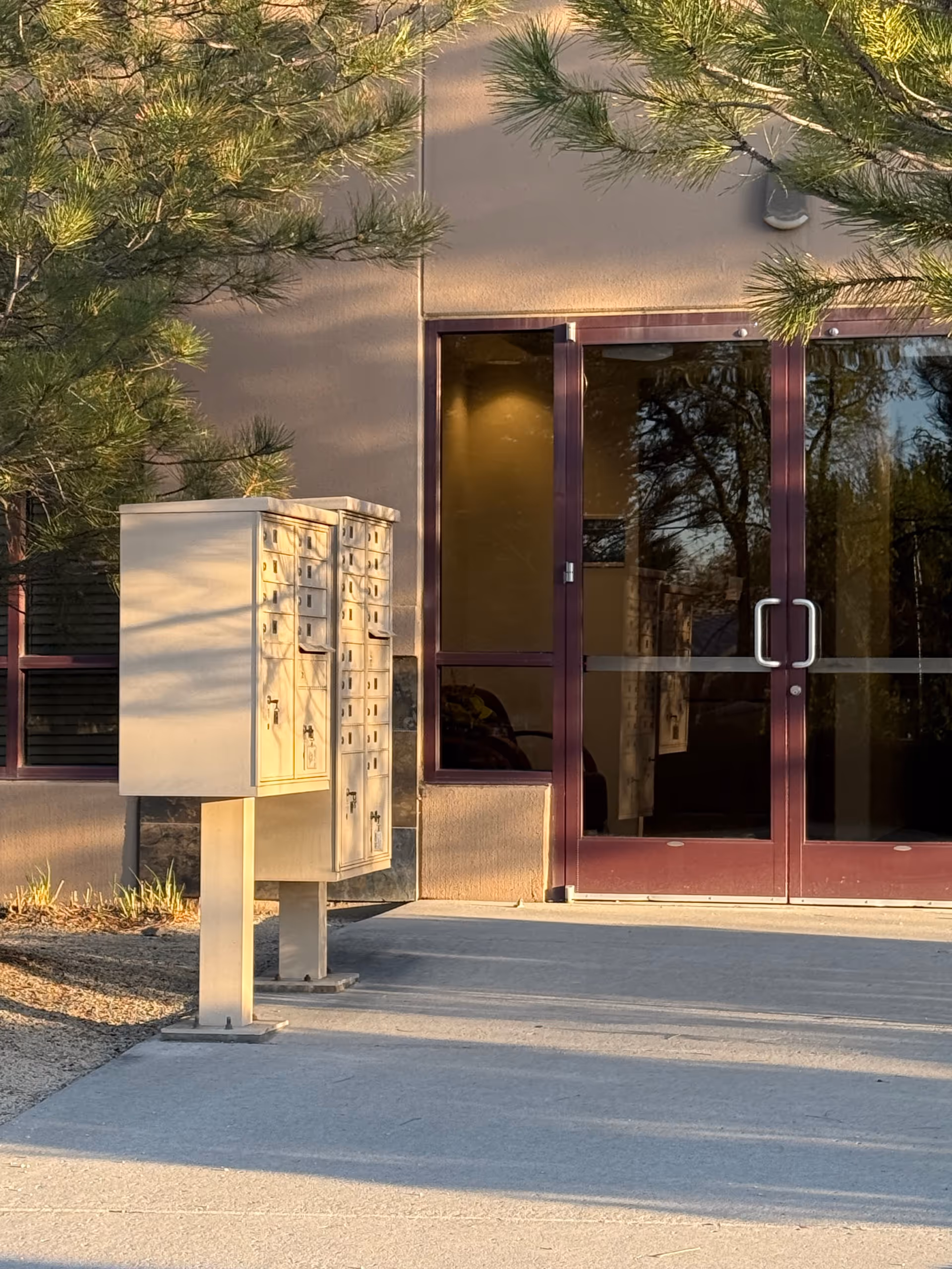 Exterior view of a facility entrance with glass doors and mailboxes.
