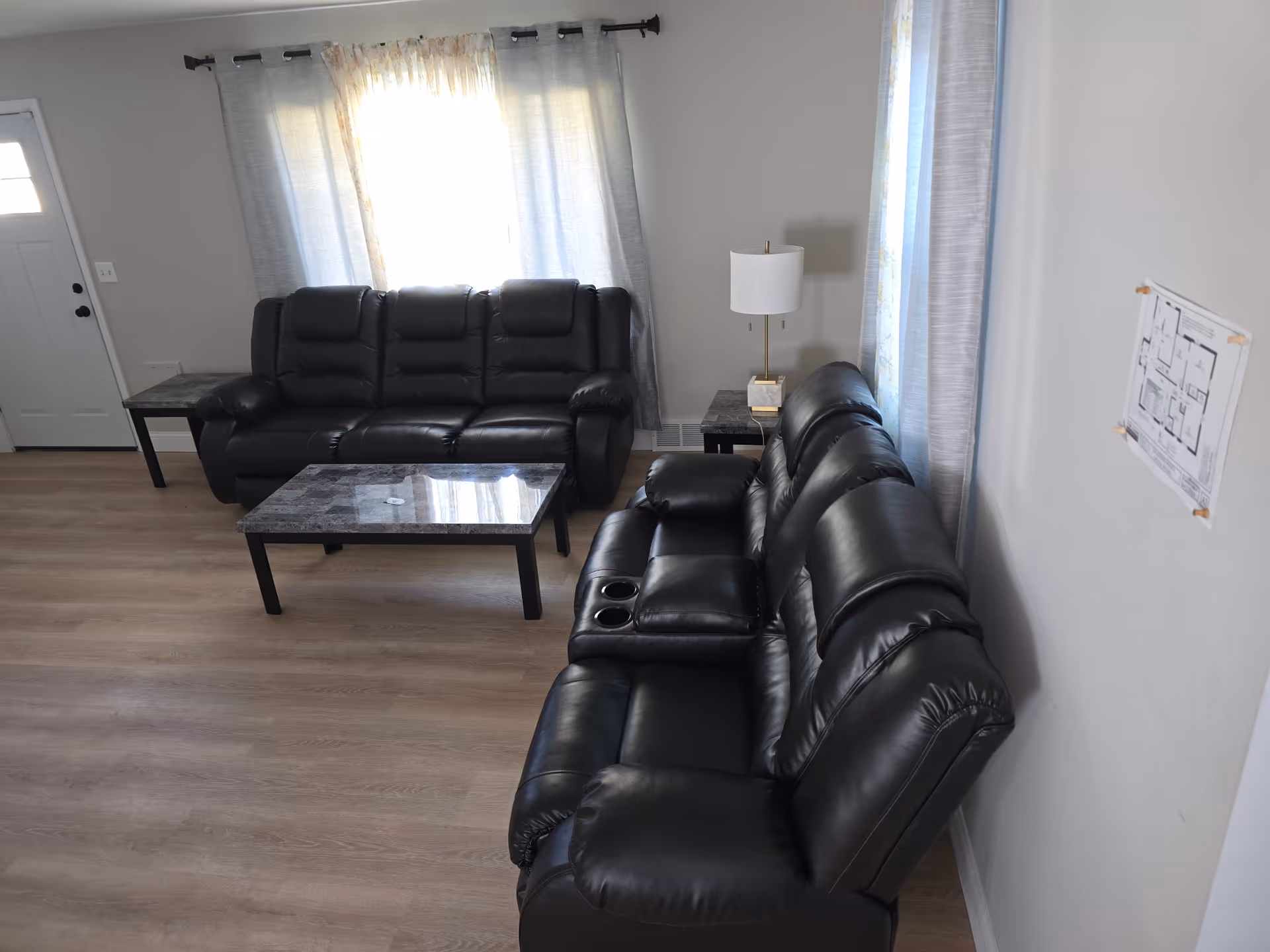 Living room in a senior facility with black leather sofas, coffee tables, and windows.