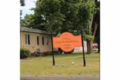 Front exterior of Orange Health Care Center with sign and trees.