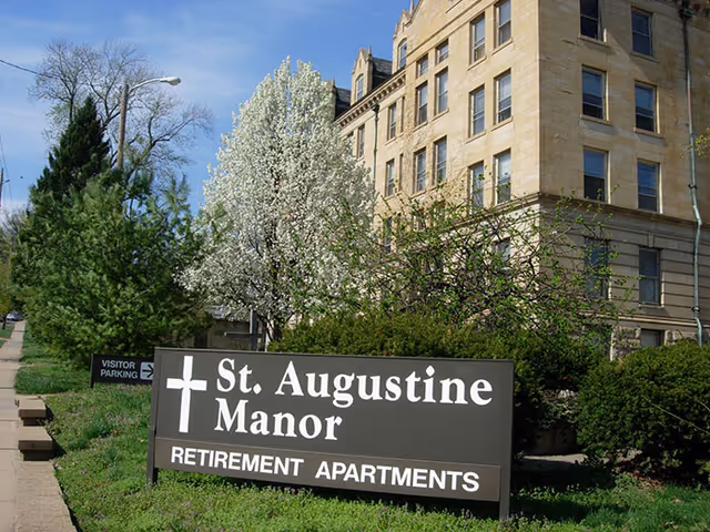 Exterior view of St Augustine Manor retirement apartments with a sign and blooming trees.