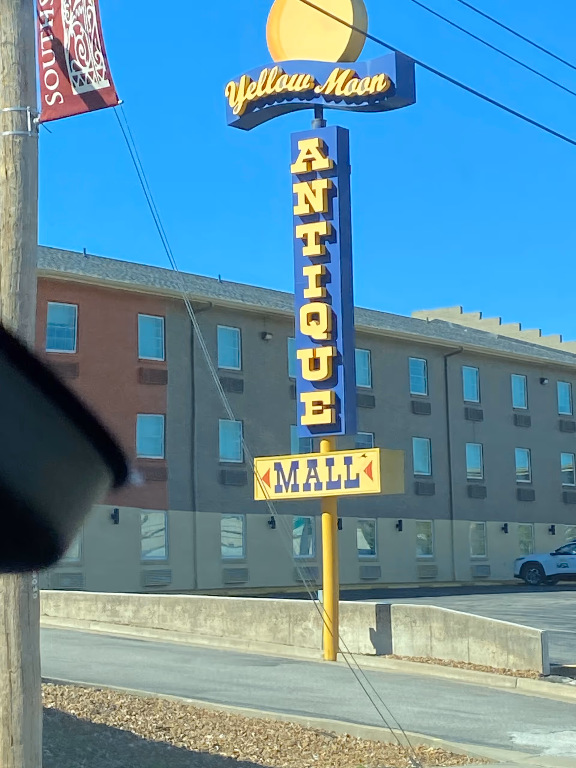Tall yellow antique mall sign beside brick building against blue sky.