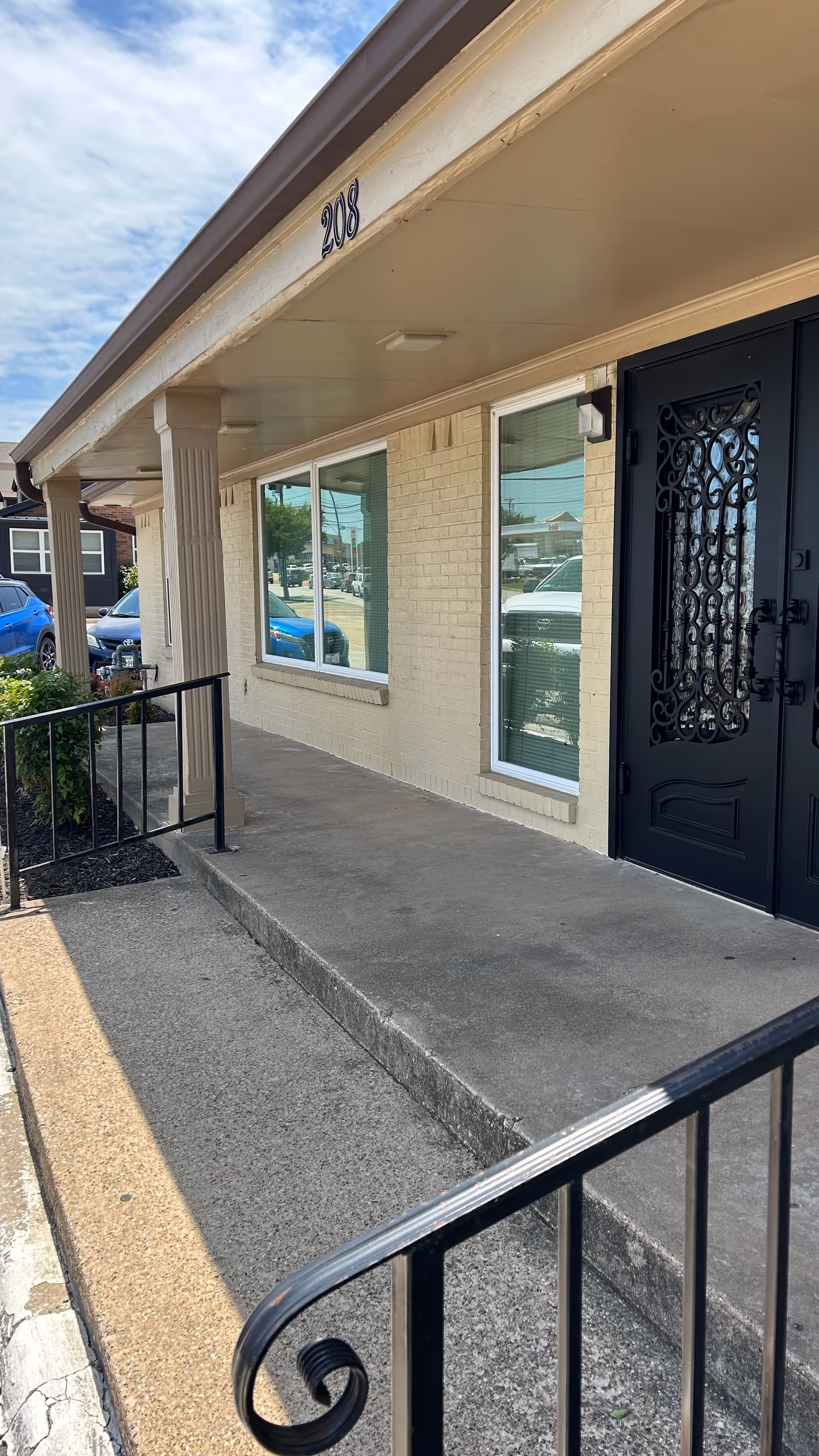 Front entrance of a beige building with glass windows and a decorative black door.