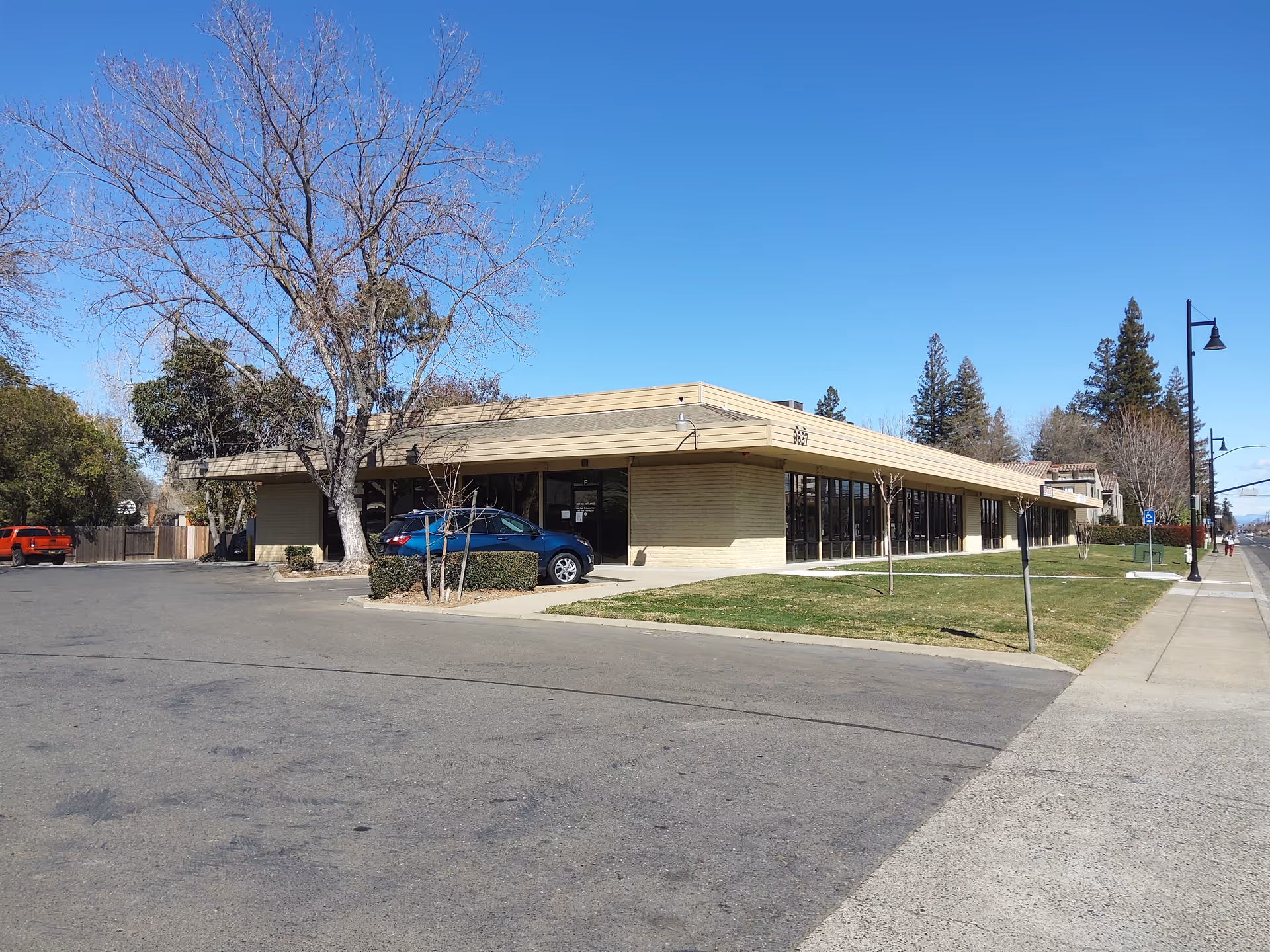 A low, beige, flat-roofed building with large front windows and a parking lot.