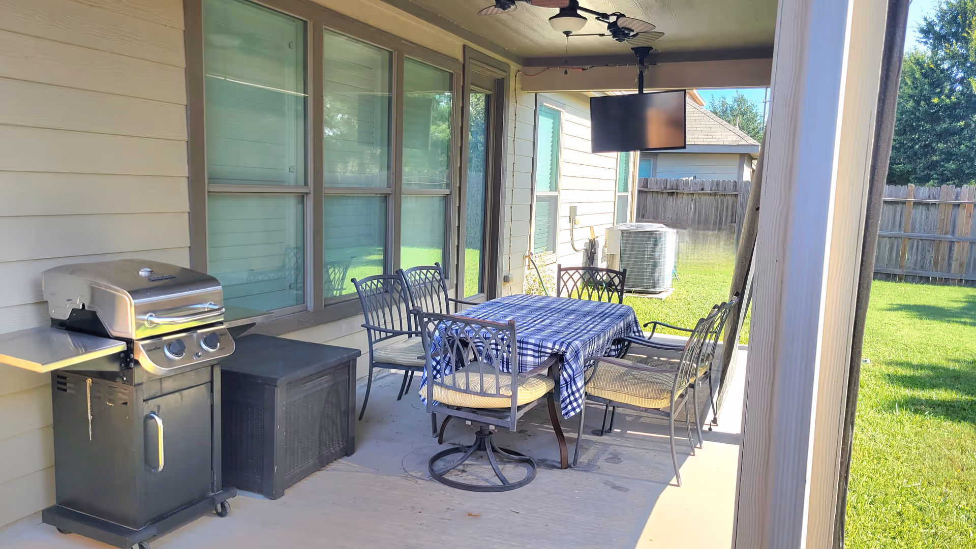 Covered outdoor patio with a dining table, six chairs, grill, and wall-mounted TV.