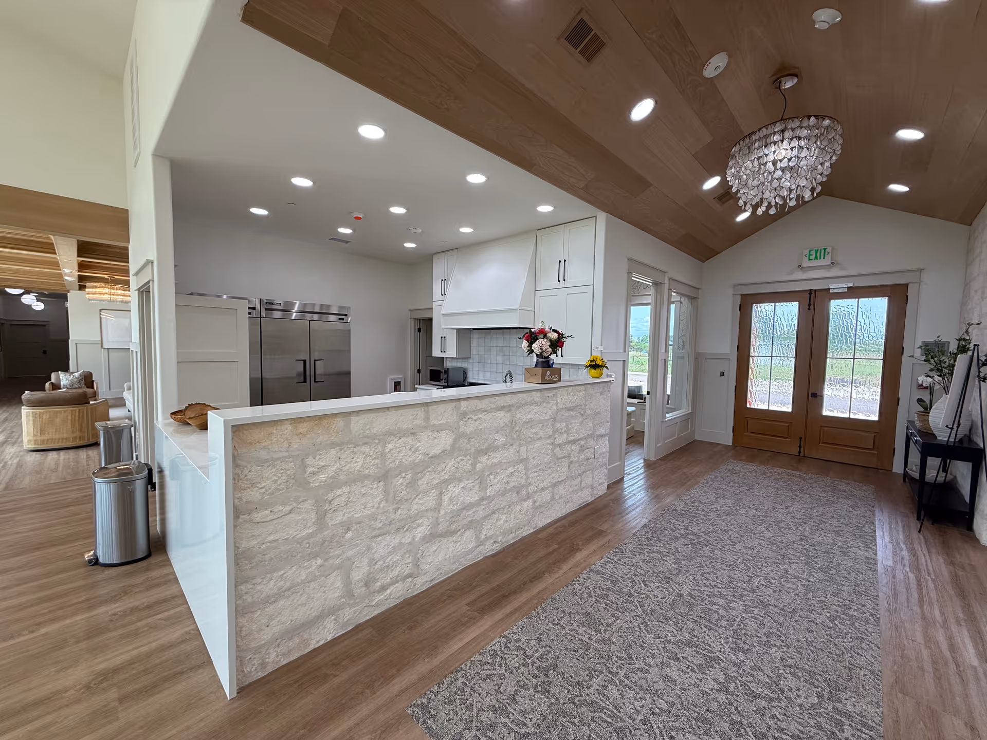 Bright modern kitchen area with a stone-front counter, white cabinets, and wooden ceiling.