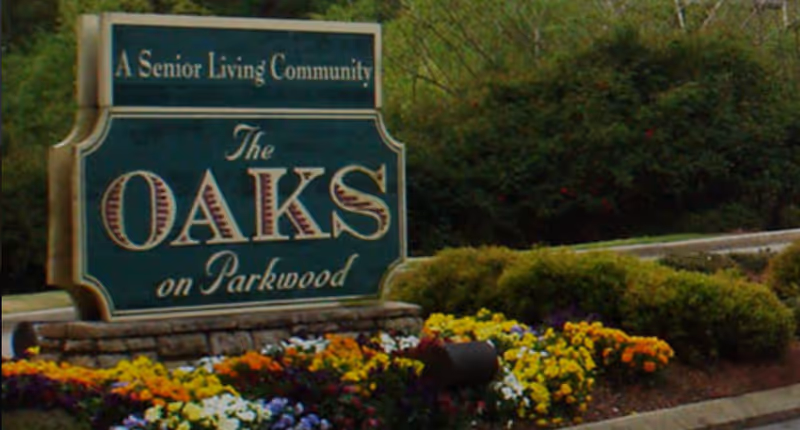Entrance sign reading "The Oaks on Parkwood" set among flowers and shrubs.