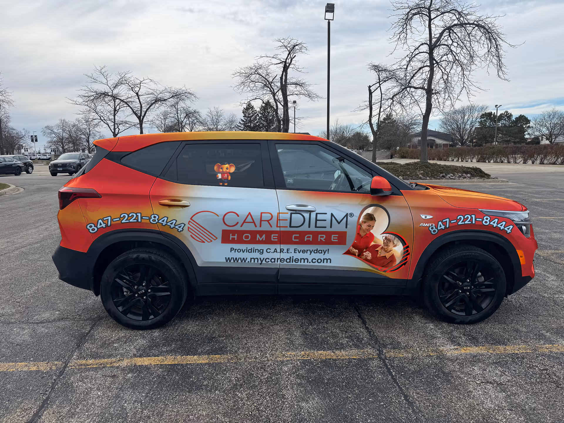 A CareDiem Home Care branded SUV parked in a lot with bare trees in background.