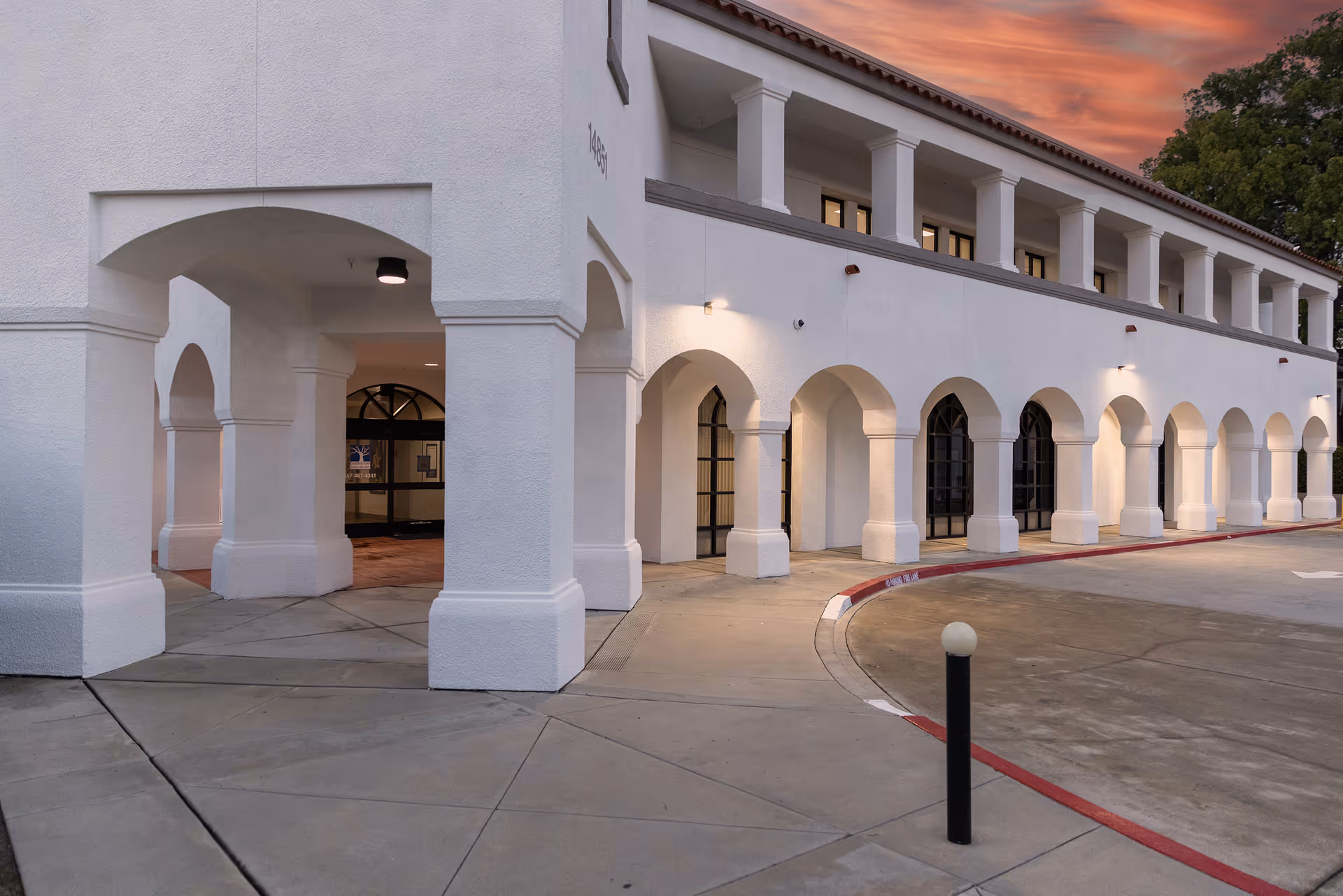 White two-story building with arches along a covered walkway at sunset